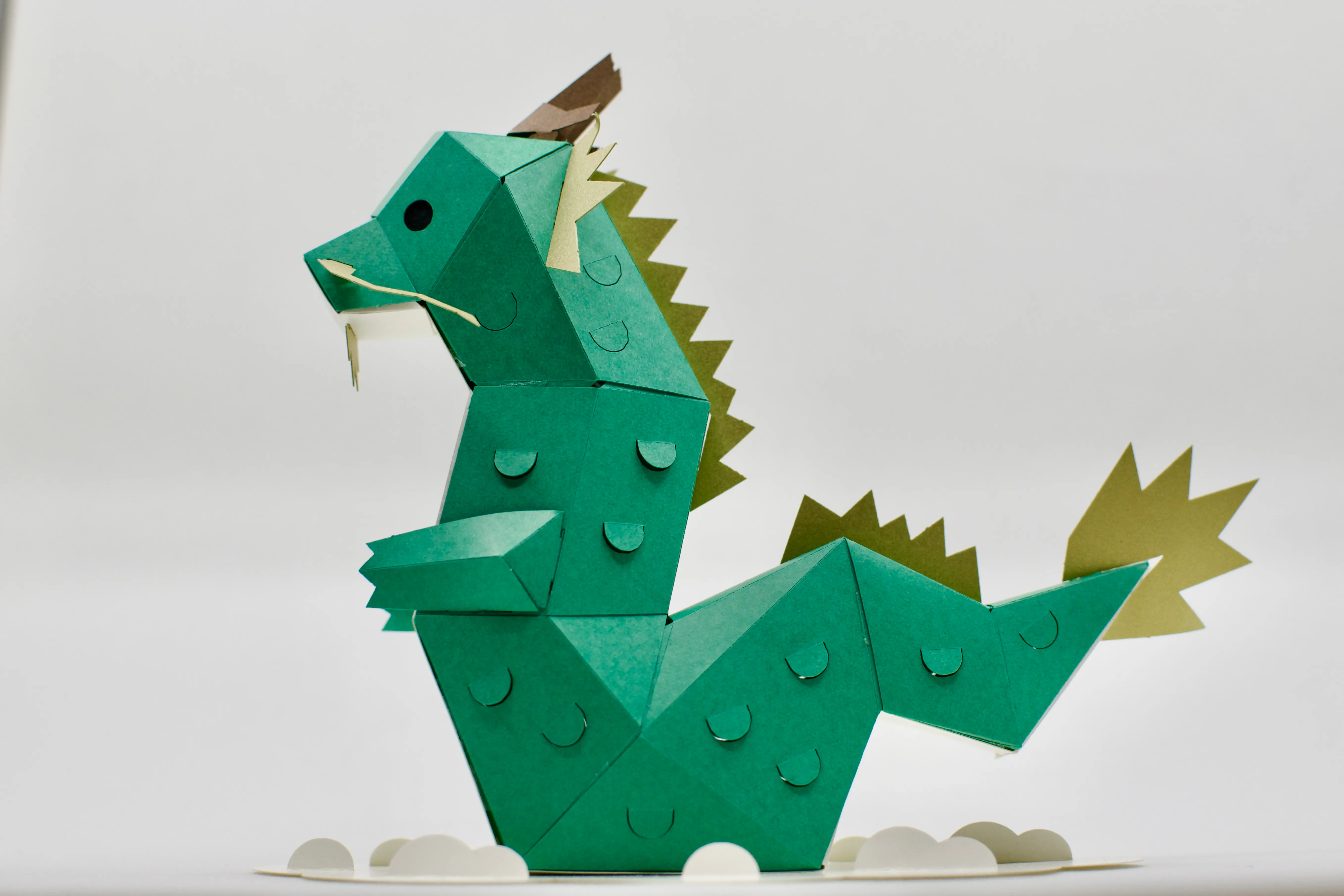 A side-on view of the papercraft dragon model sitting on top of a paper “cloud”