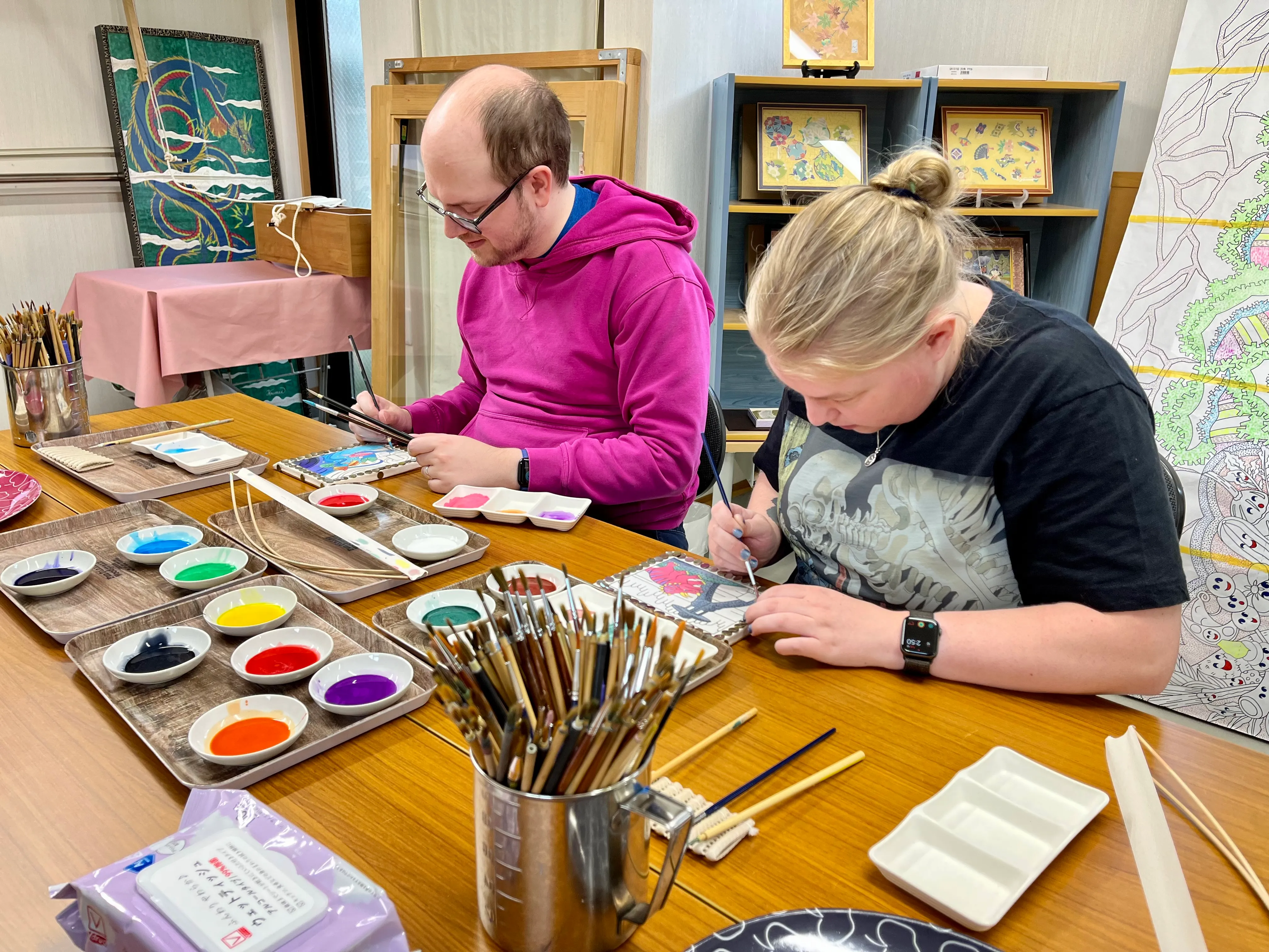 Ross and Leah with paintbrushes in hand, concentrating on applying dye to their yūzen pieces
