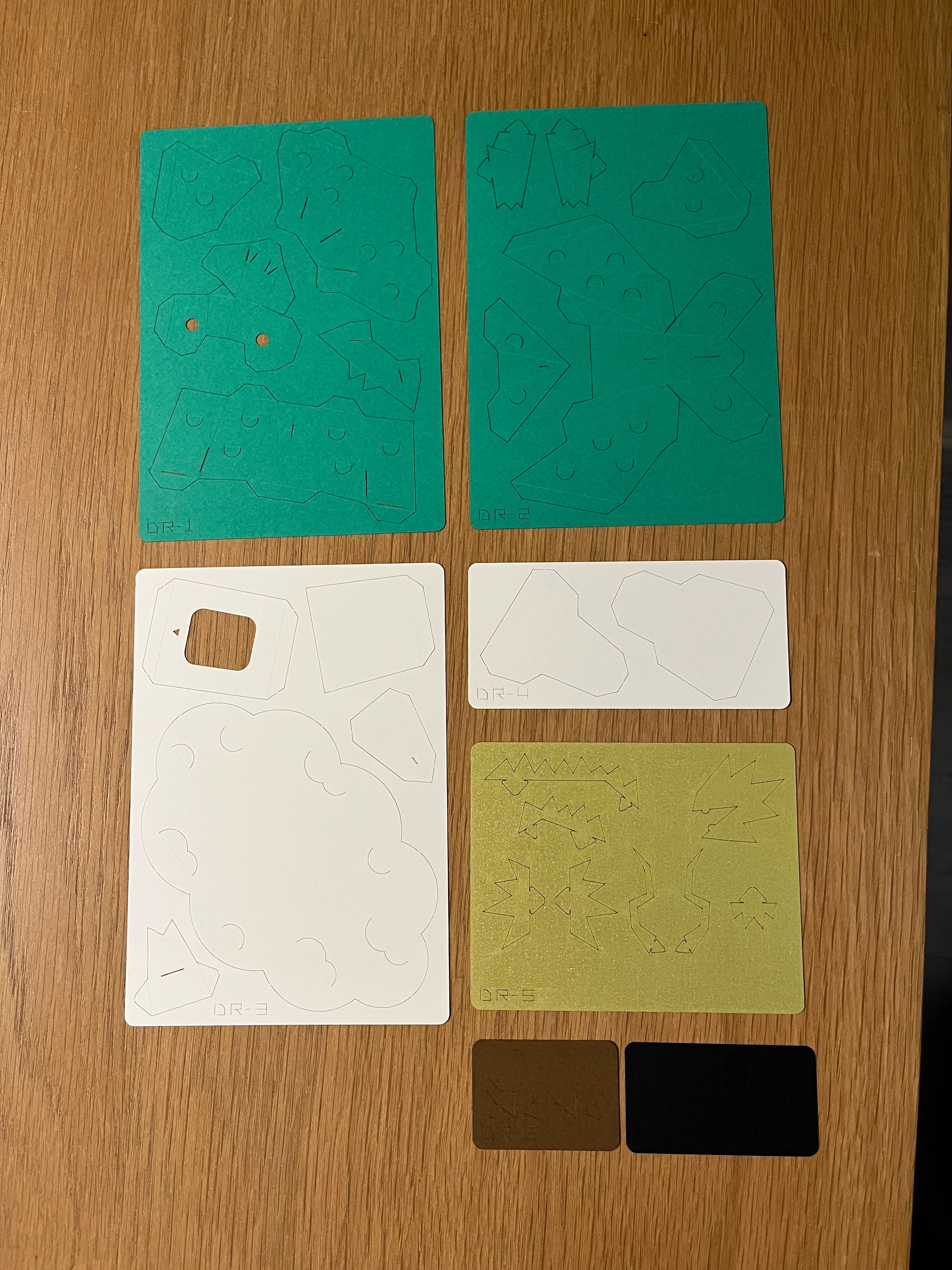 Green, white, gold, black, and brown pieces of paper with perforated polygons