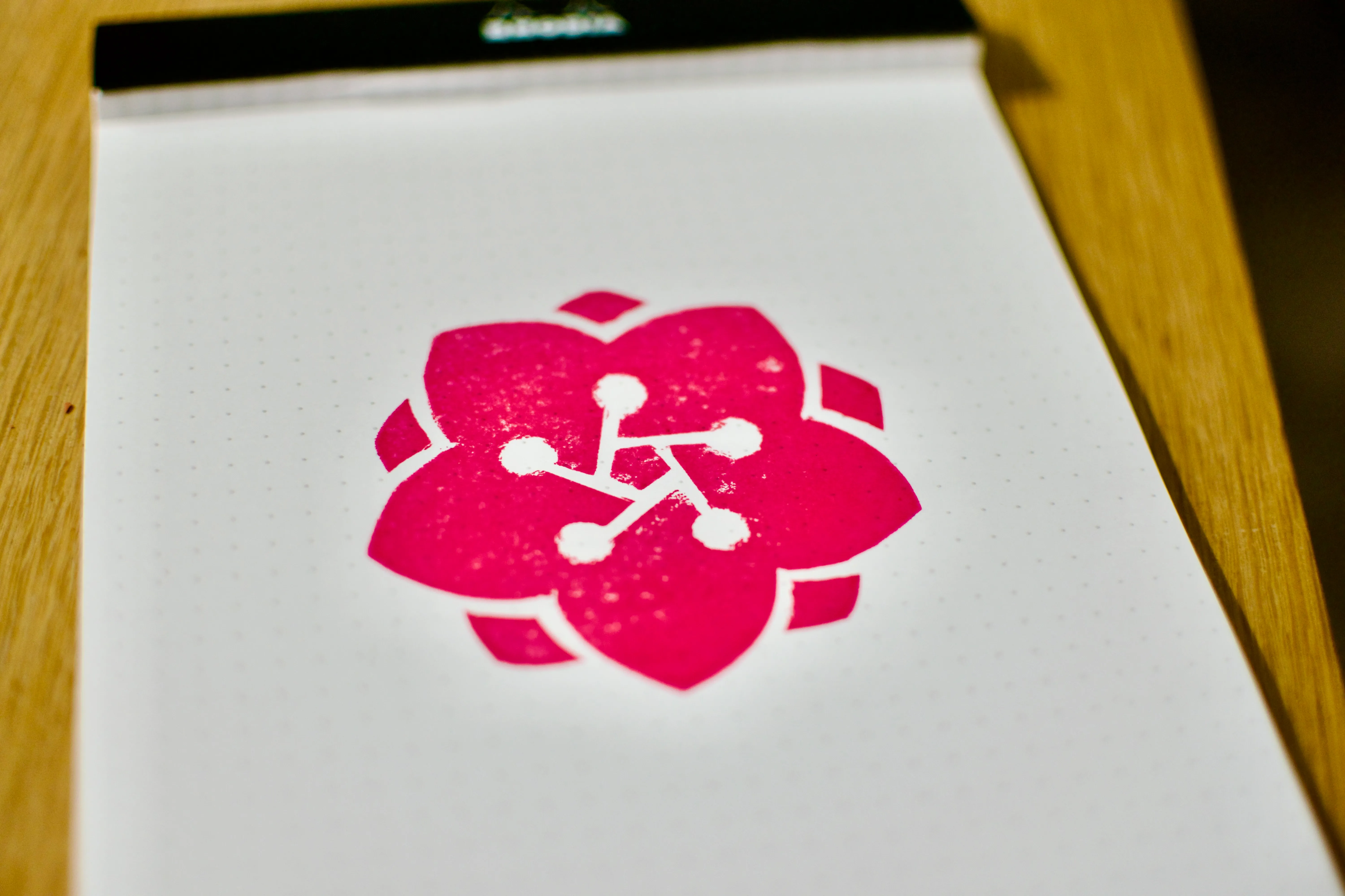 A stamp impression in fuchsia ink of a stylized rose, with five petals and five stamens emanating from a pentagonal center