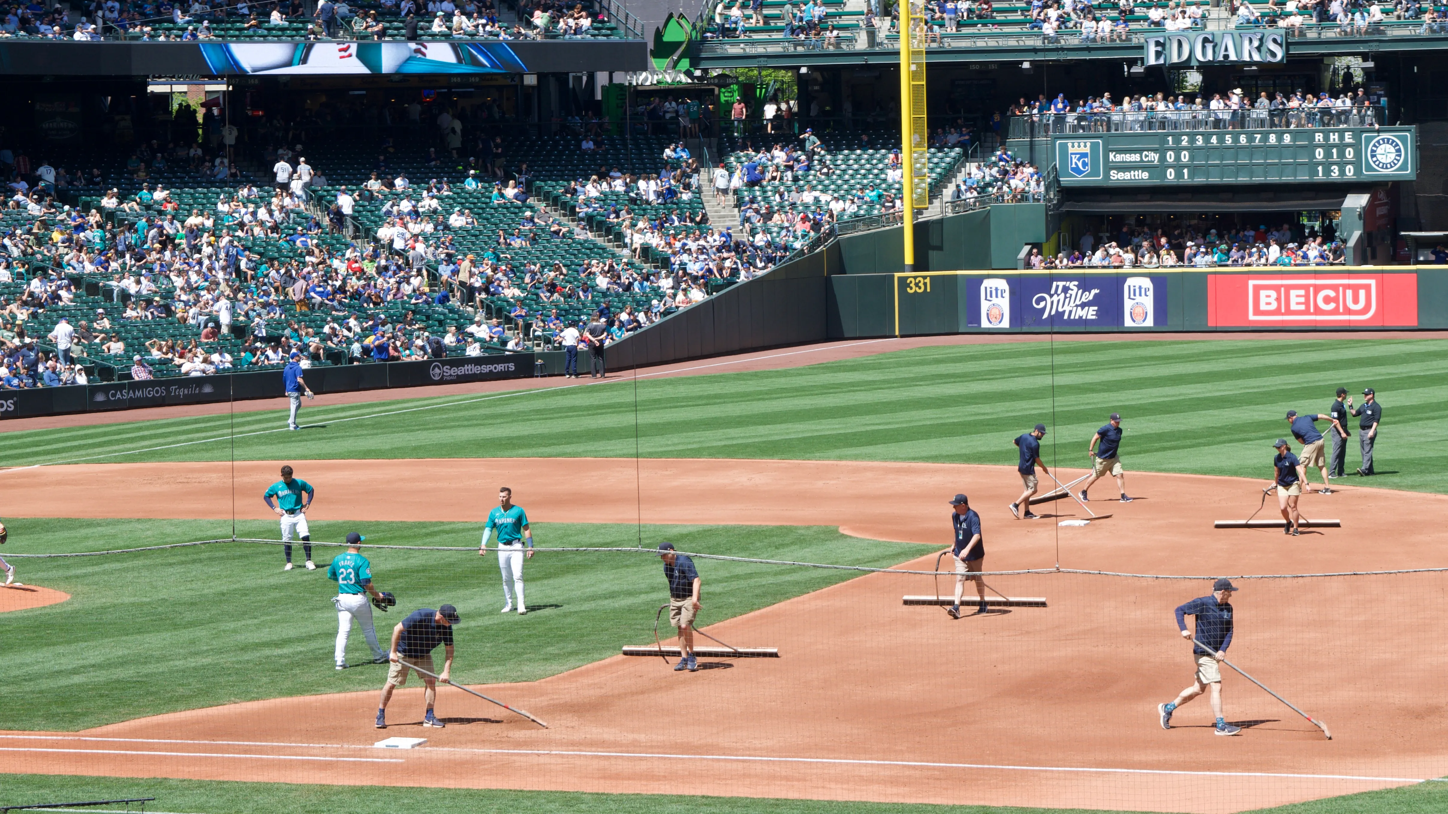 People with large rakes smooth out the dirt between first and second base