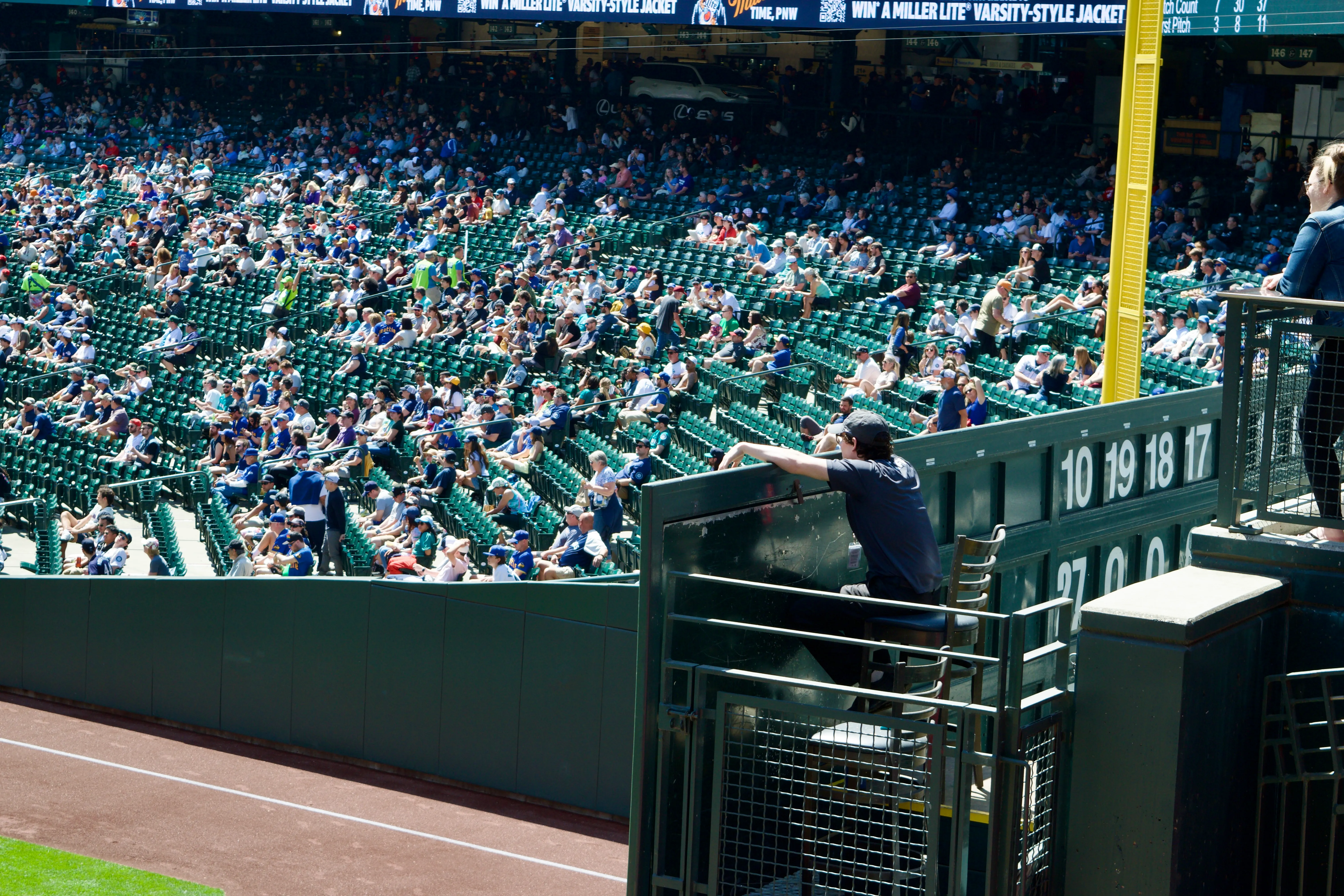 A young, bored-looking person sits on a chair and rests their arms on the stadium scoreboard