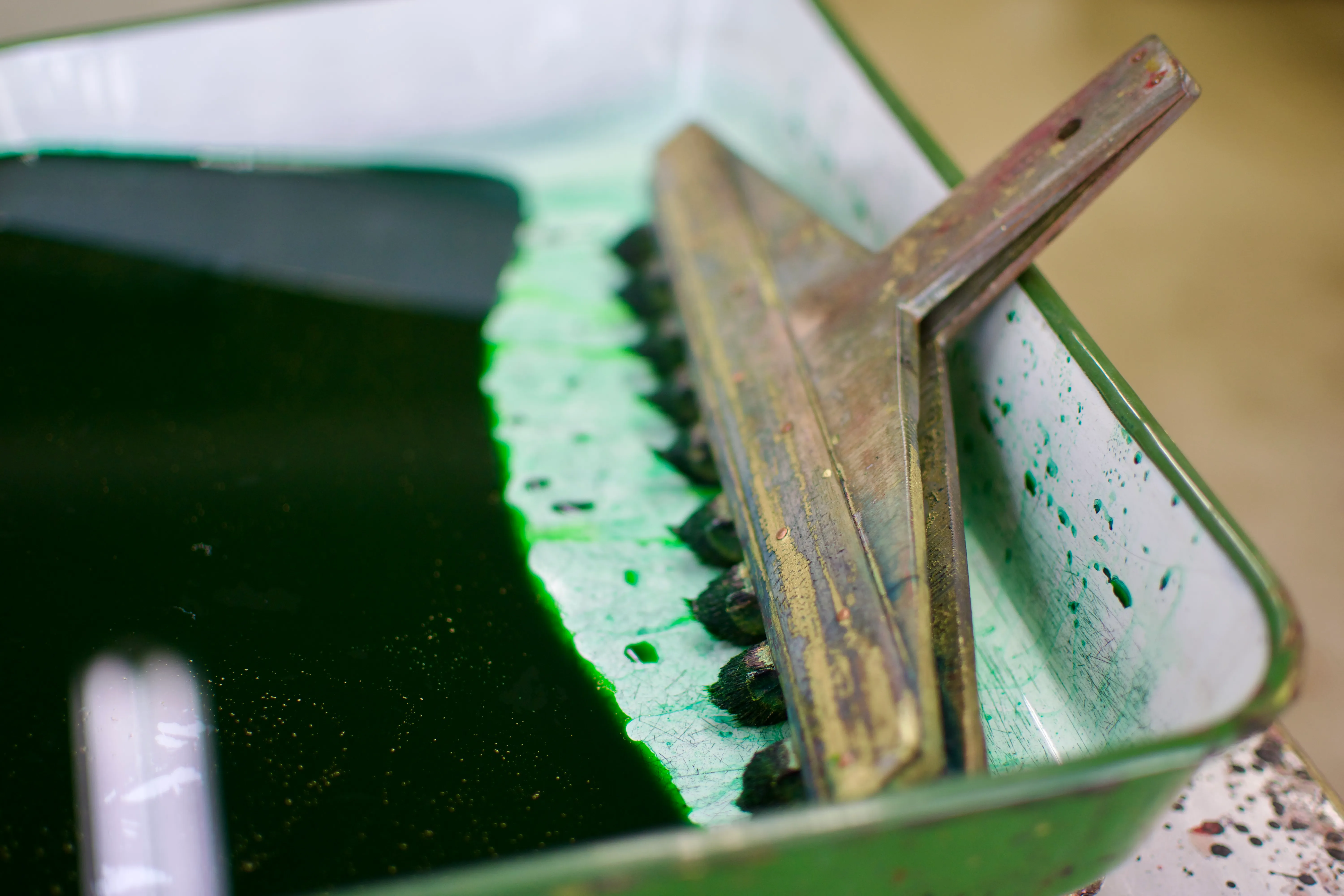 A paintbrush with many heads, used to paint stripes, sits in a pan of green paint