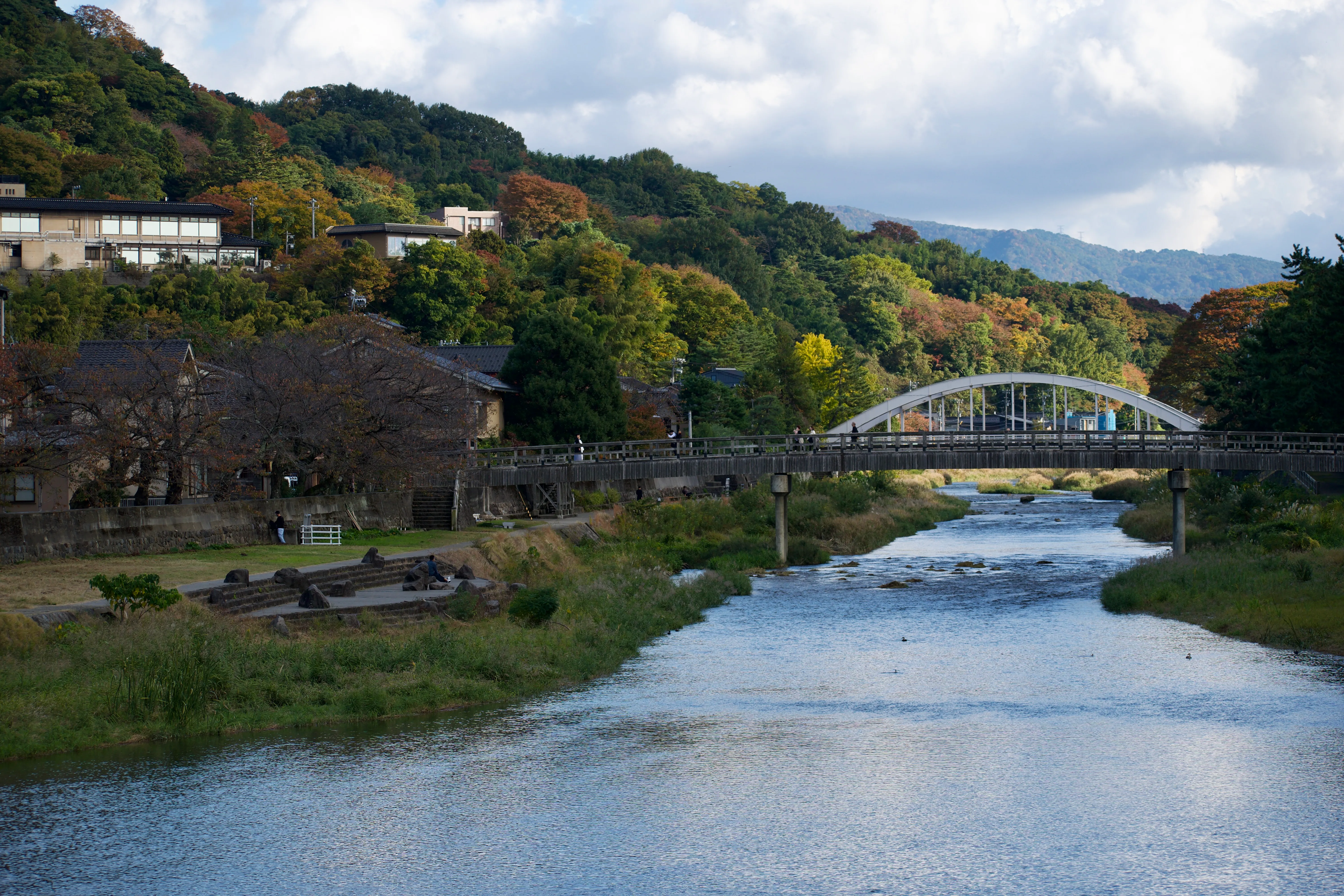 A wooden bridge spans a river, with autumn leaves in the background