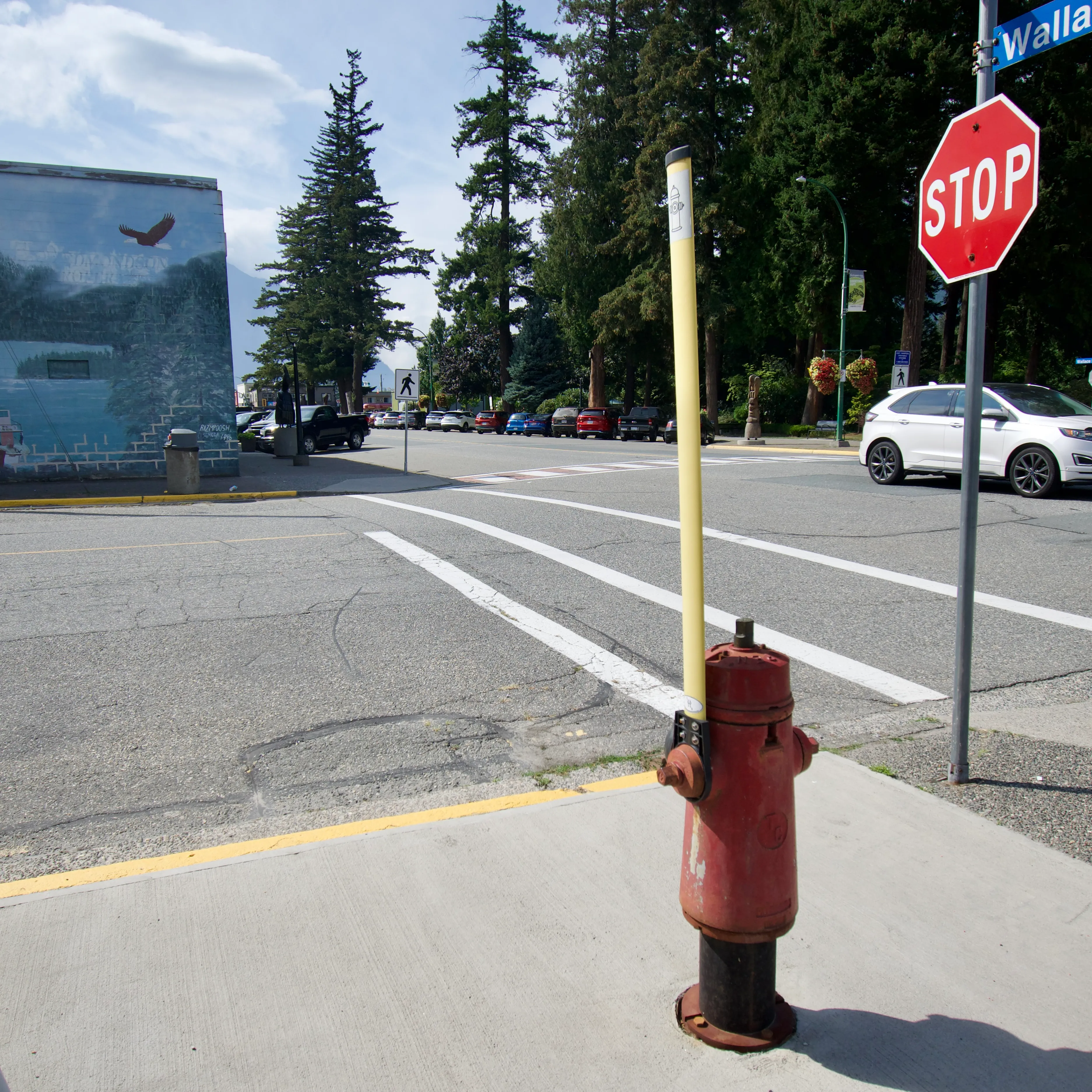 A red fire hydrant on a street corner with a yellow antenna attached