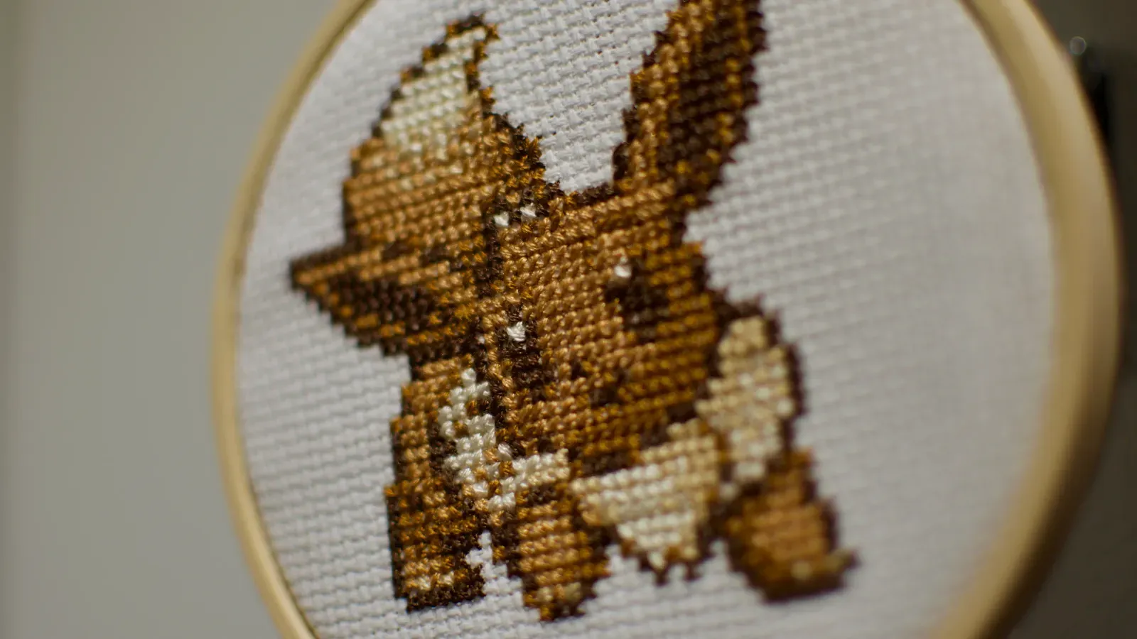 A small cross-stitch of the evolution Pokémon Eevee against a white background