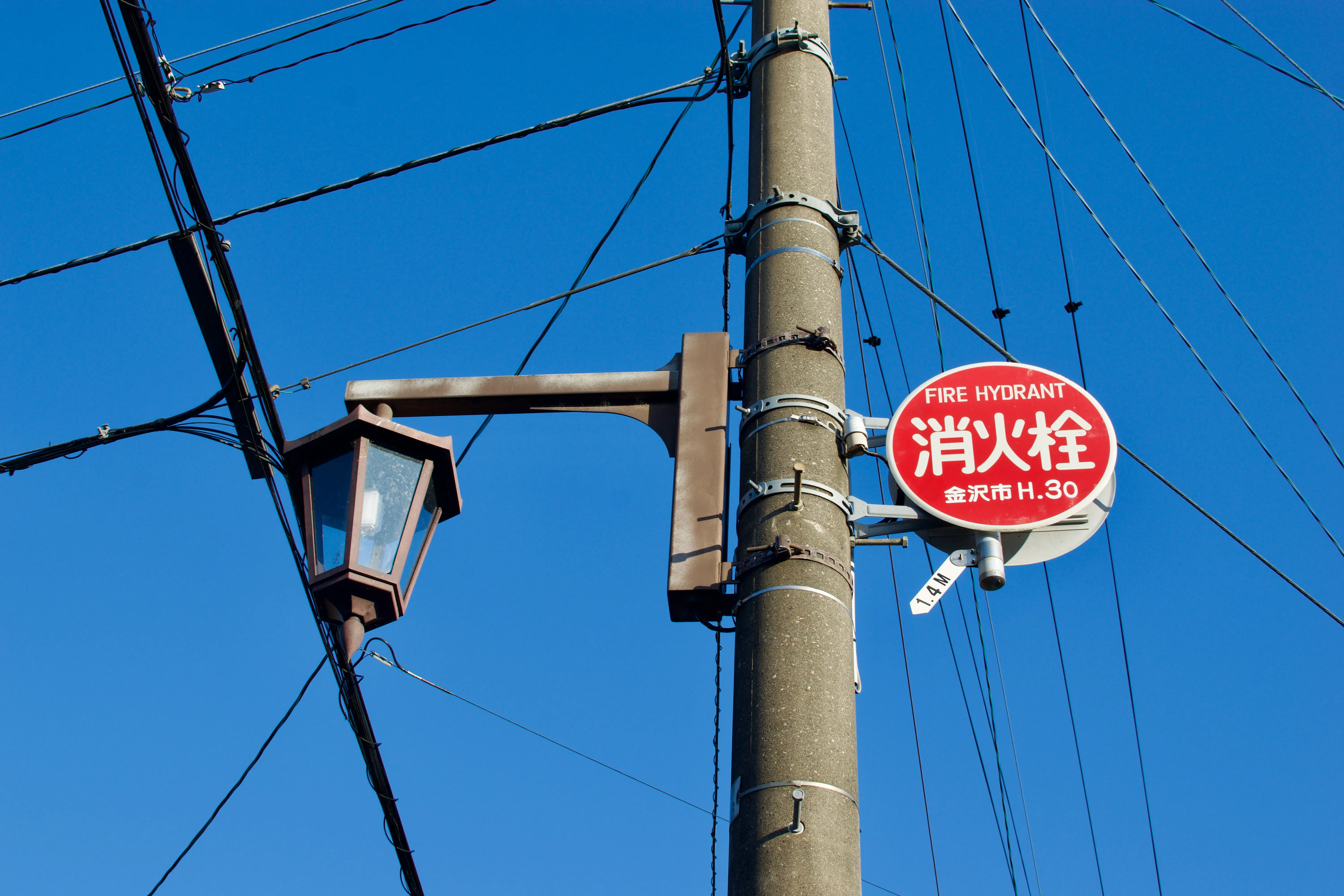 A Japanese sign attached to a telephone pole points to a fire hydrant below