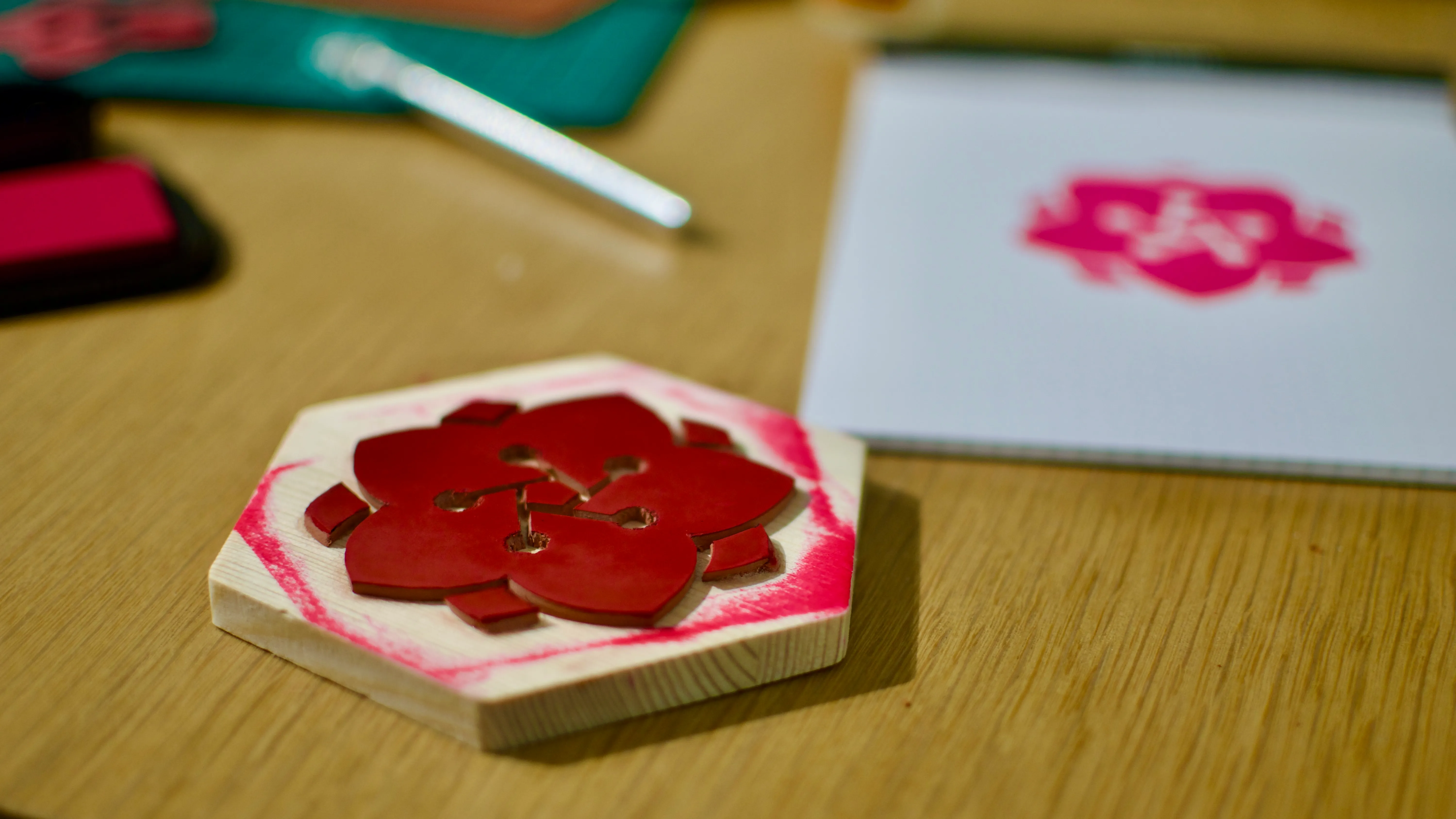 A homemade rubber stamp in the foreground, with stampmaking supplies and a test print in the background