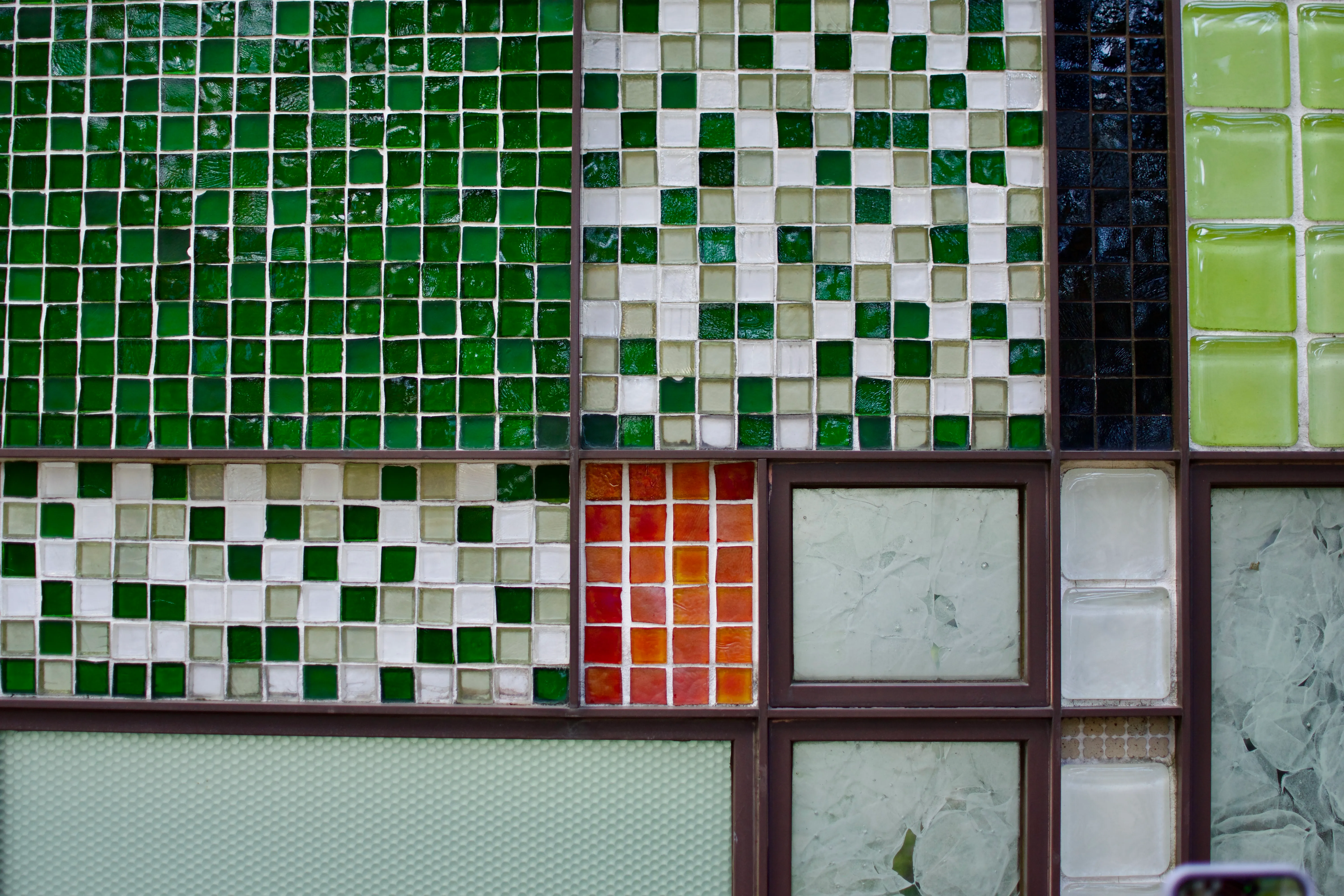 A tile mosaic featuring rectangular sections of different patterns. Some sections are built from green and white square tiles; others have interesting patterns in larger panes of partly-frosted glass.