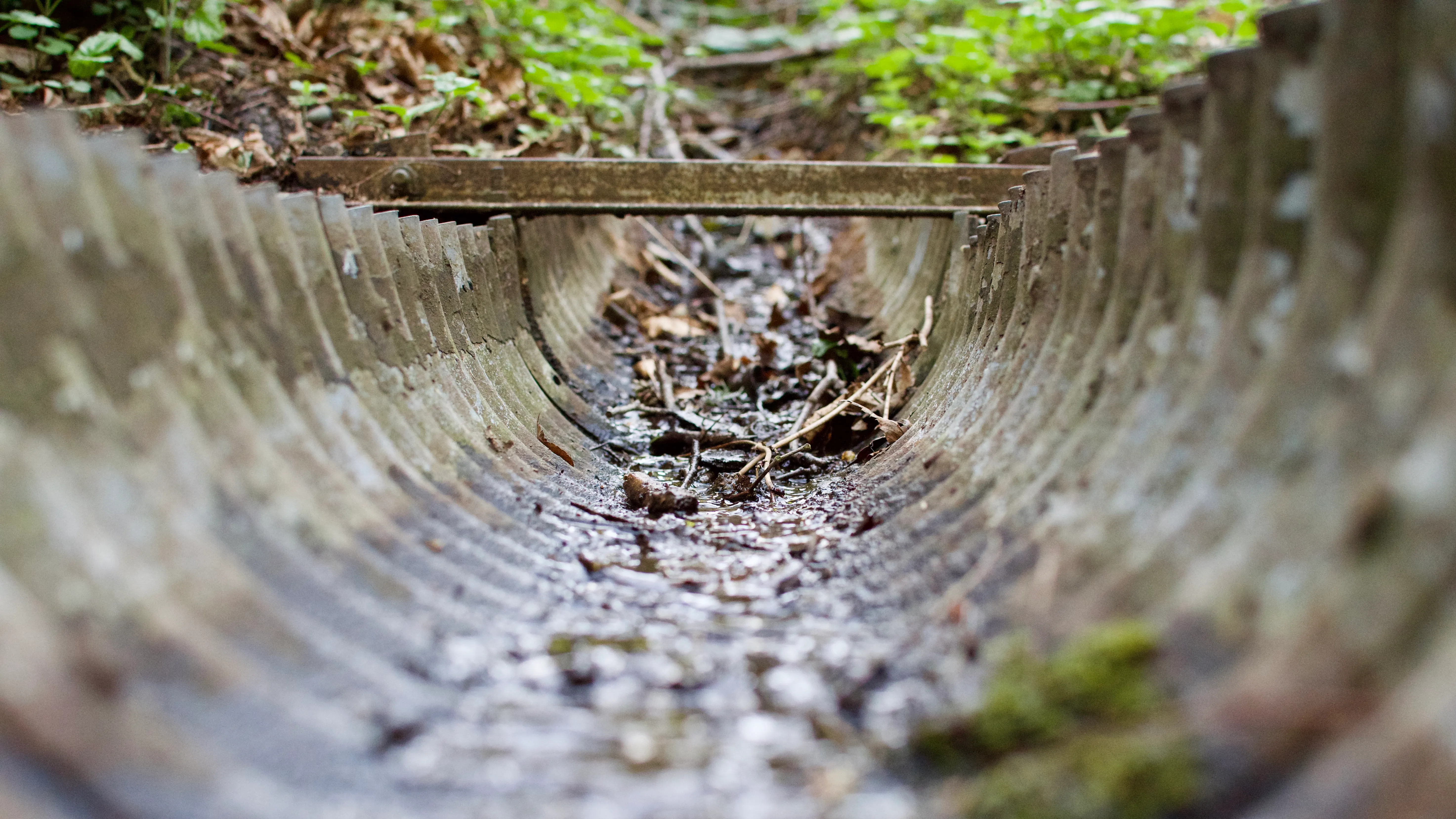 Inside a small drainage channel filled with water and debris. The channel's metal walls are textured with ridges.