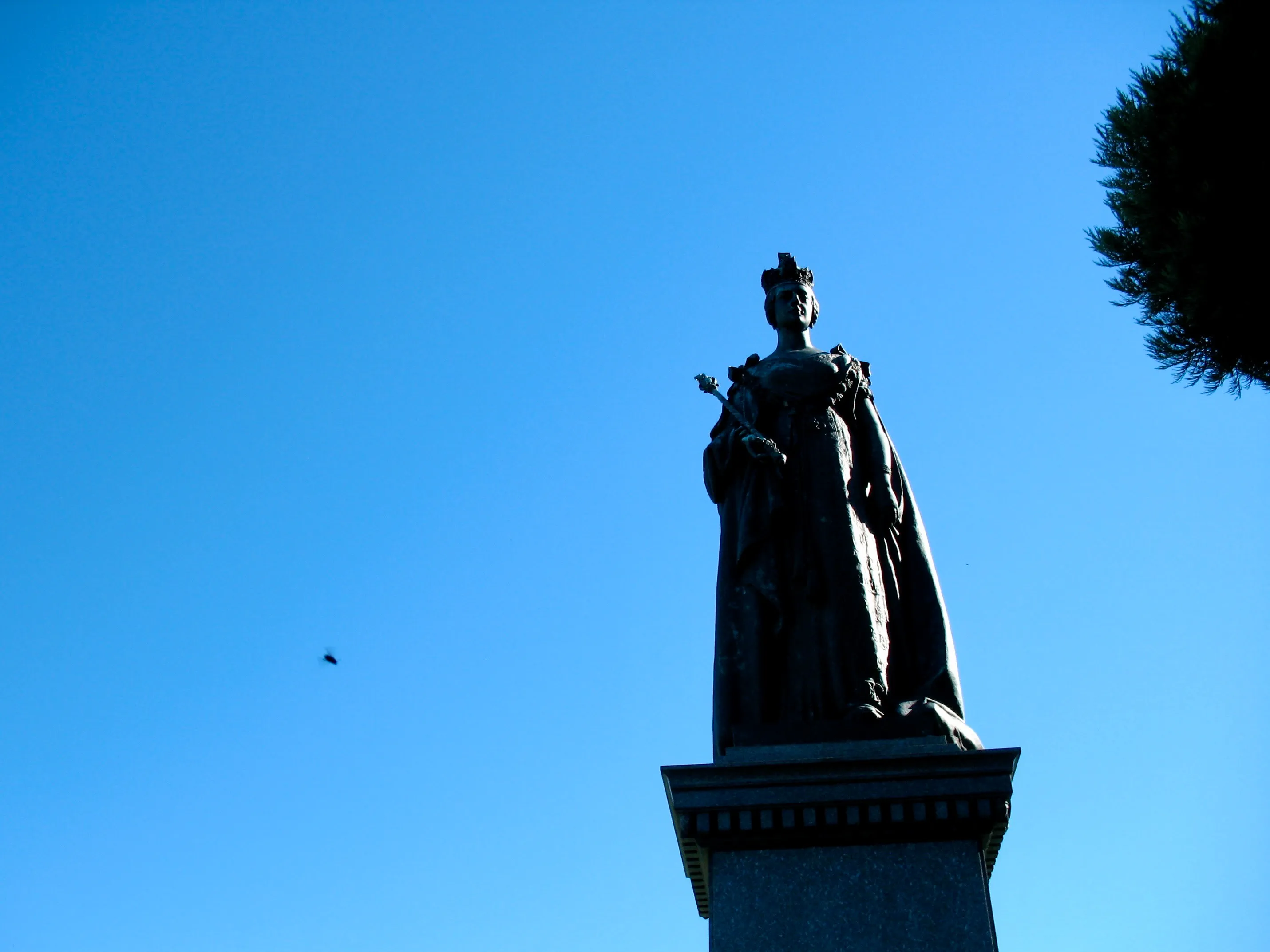 A statue of Queen Victoria, almost in silhouette, against a clear blue sky