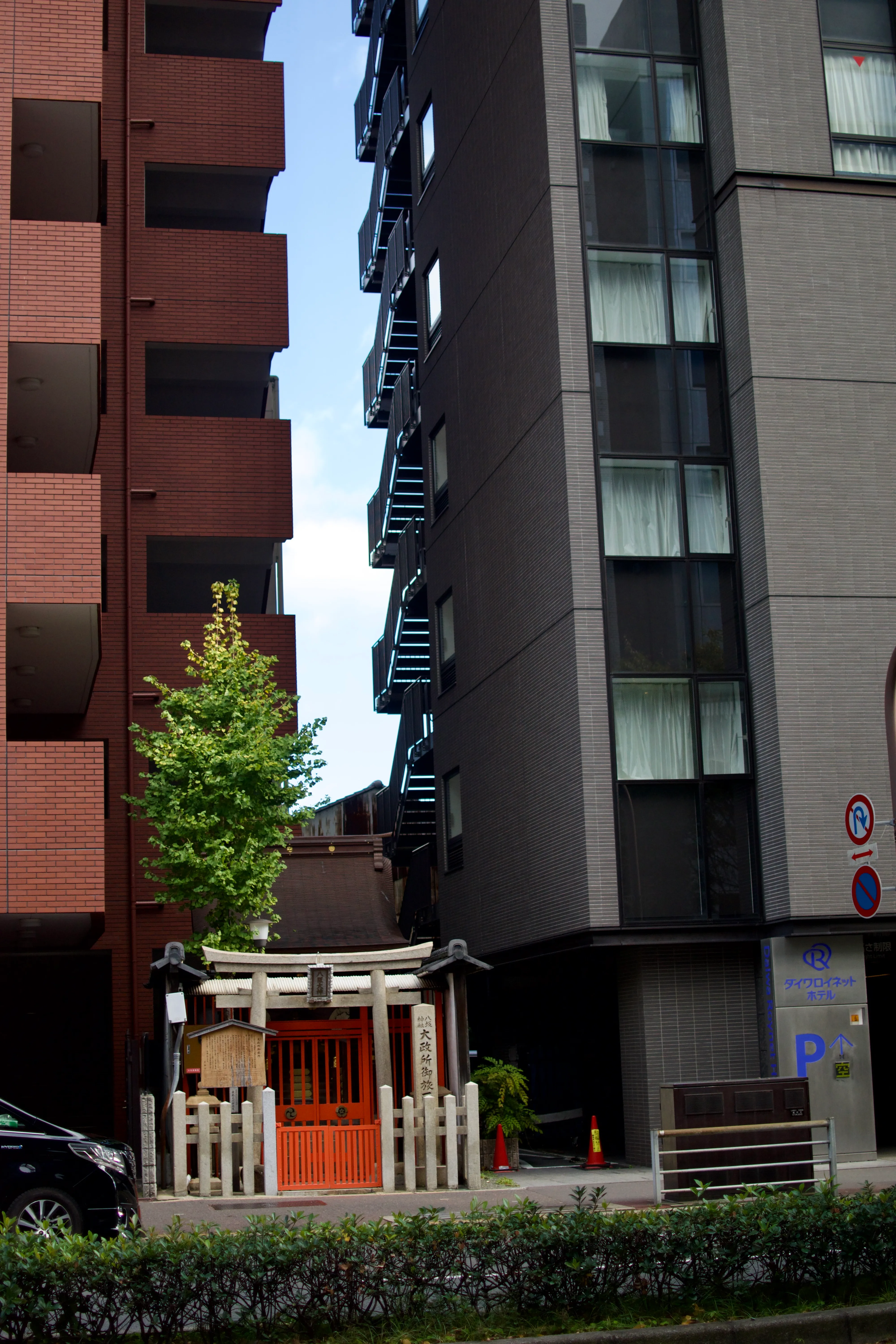 A small shinto shrine building nestled between two tall apartment buildings