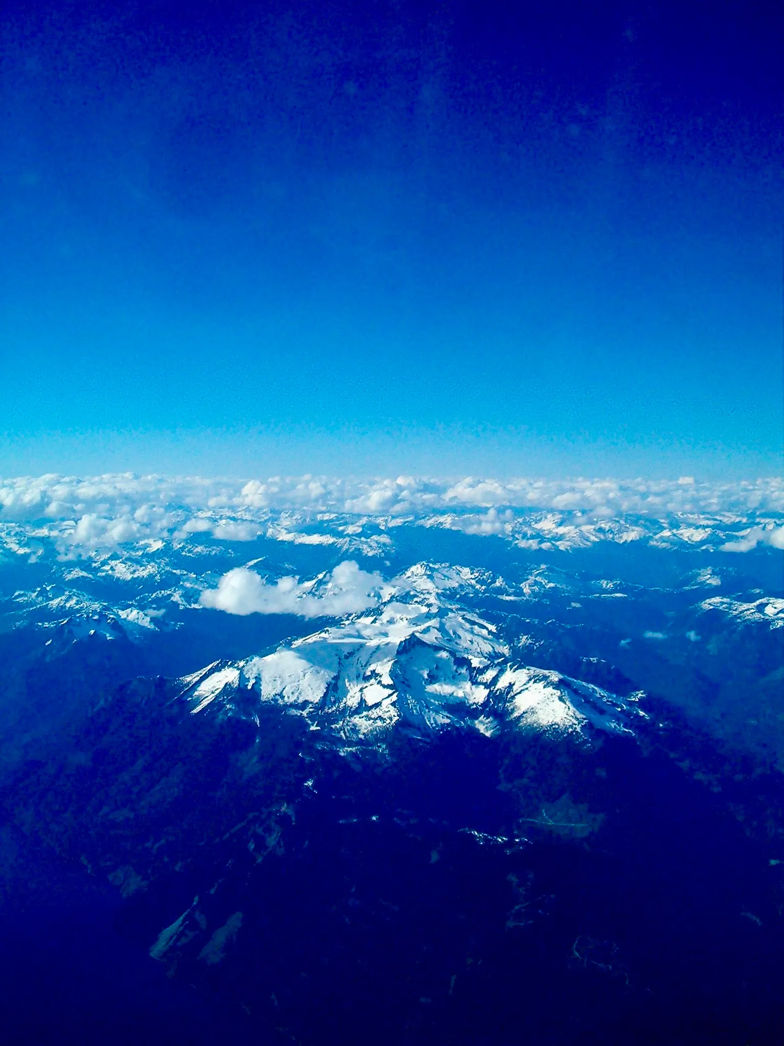 A snow-covered mountain viewed from above. White clouds partially obscure the peak.