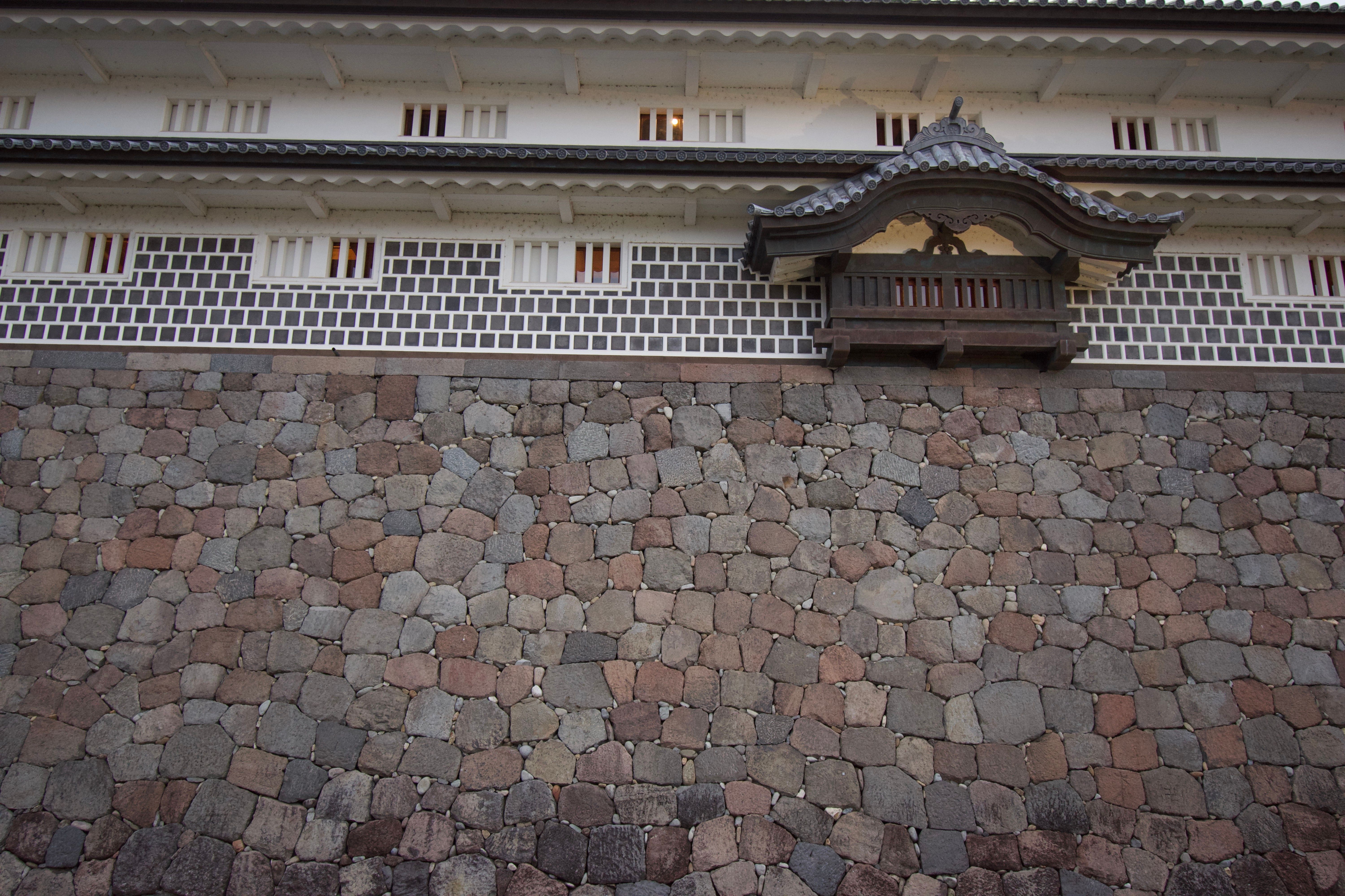 The stone foundation of a Japanese castle and the white lower walls of the keep. One of the keep windows is decorated with an ornate gable.