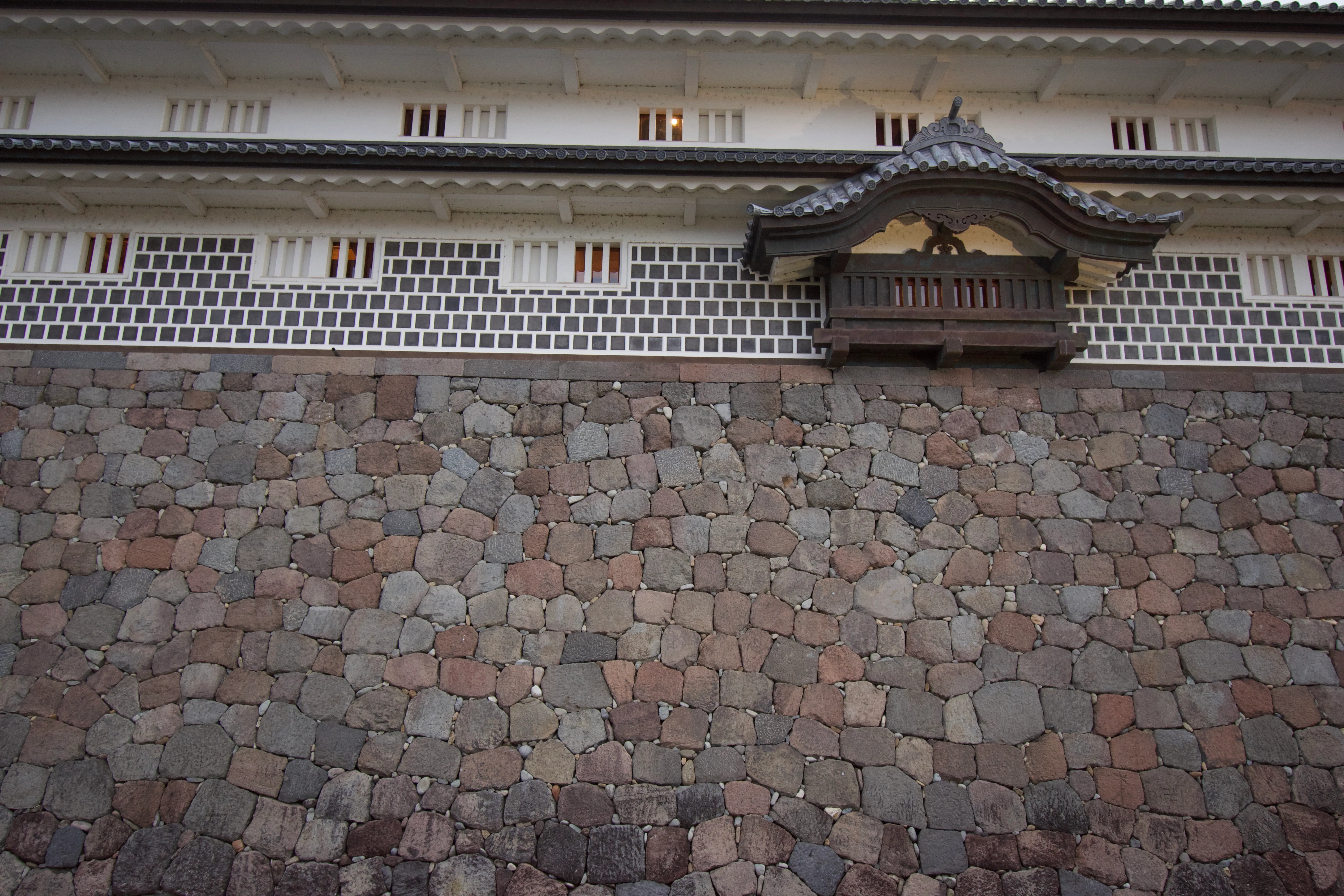 The stone foundation of a Japanese castle and the white lower walls of the keep. One of the keep windows is decorated with an ornate gable.