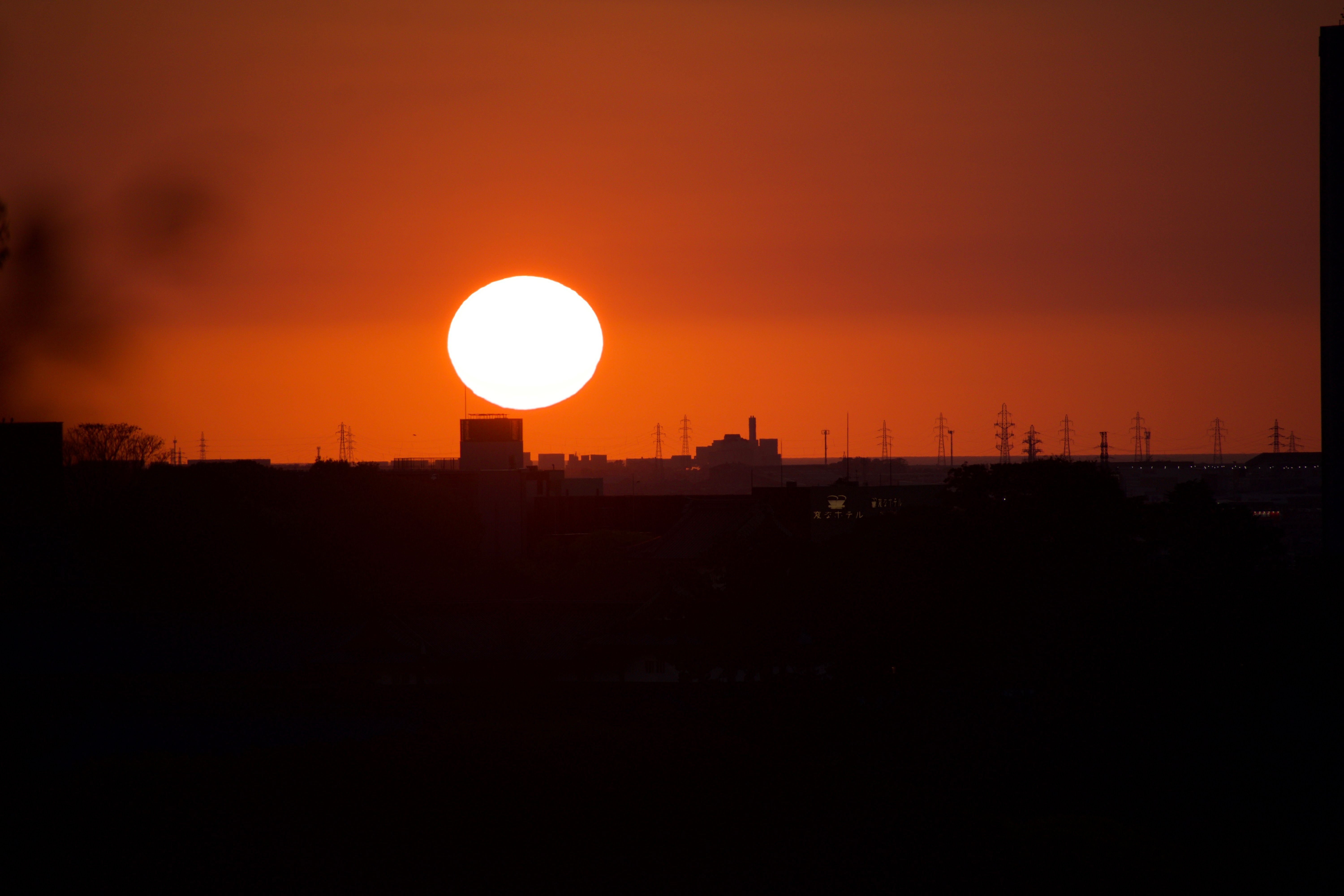 A bright orange sun sets behind a city skyline