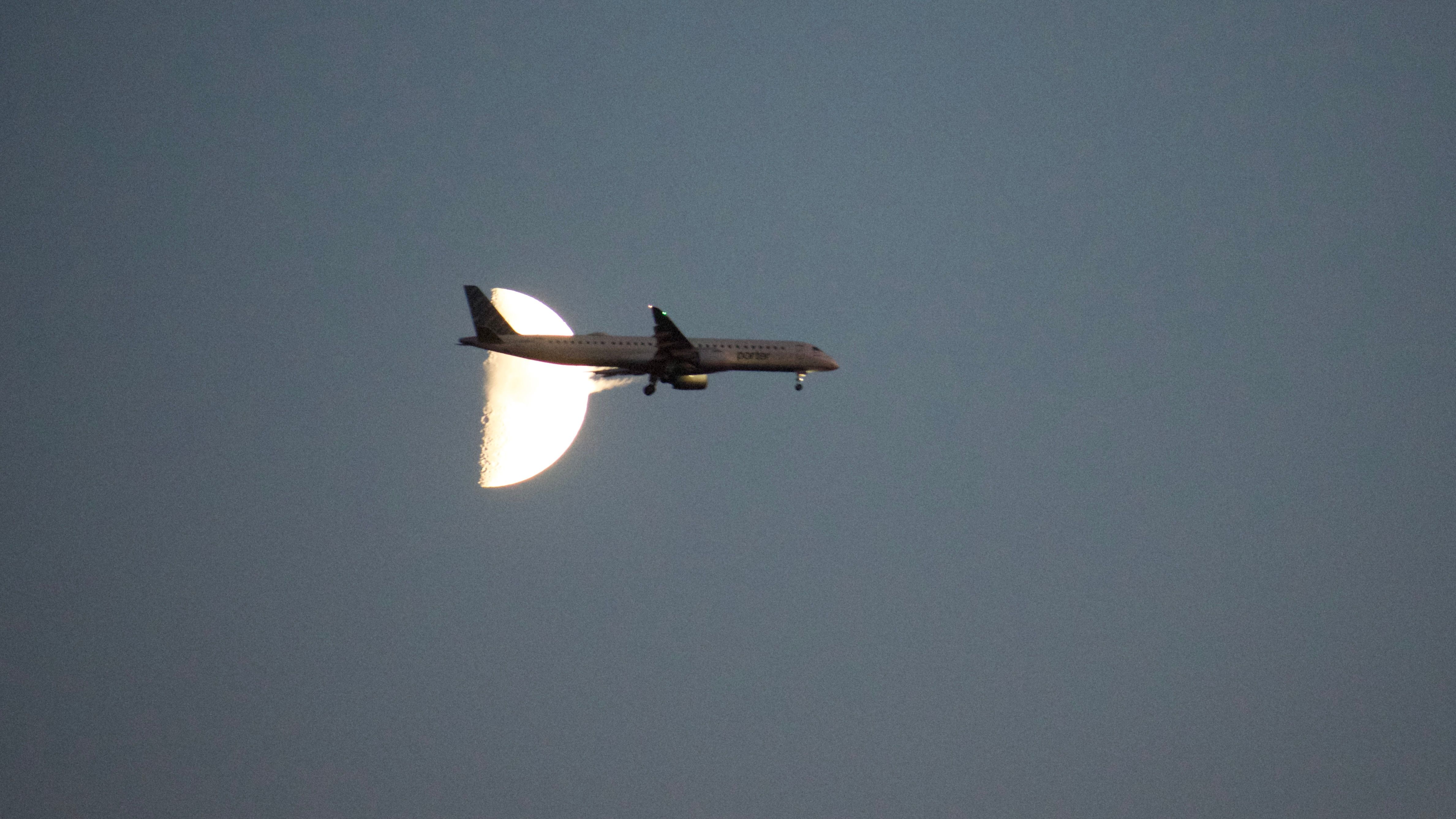 A plane passes in front of a quarter-moon