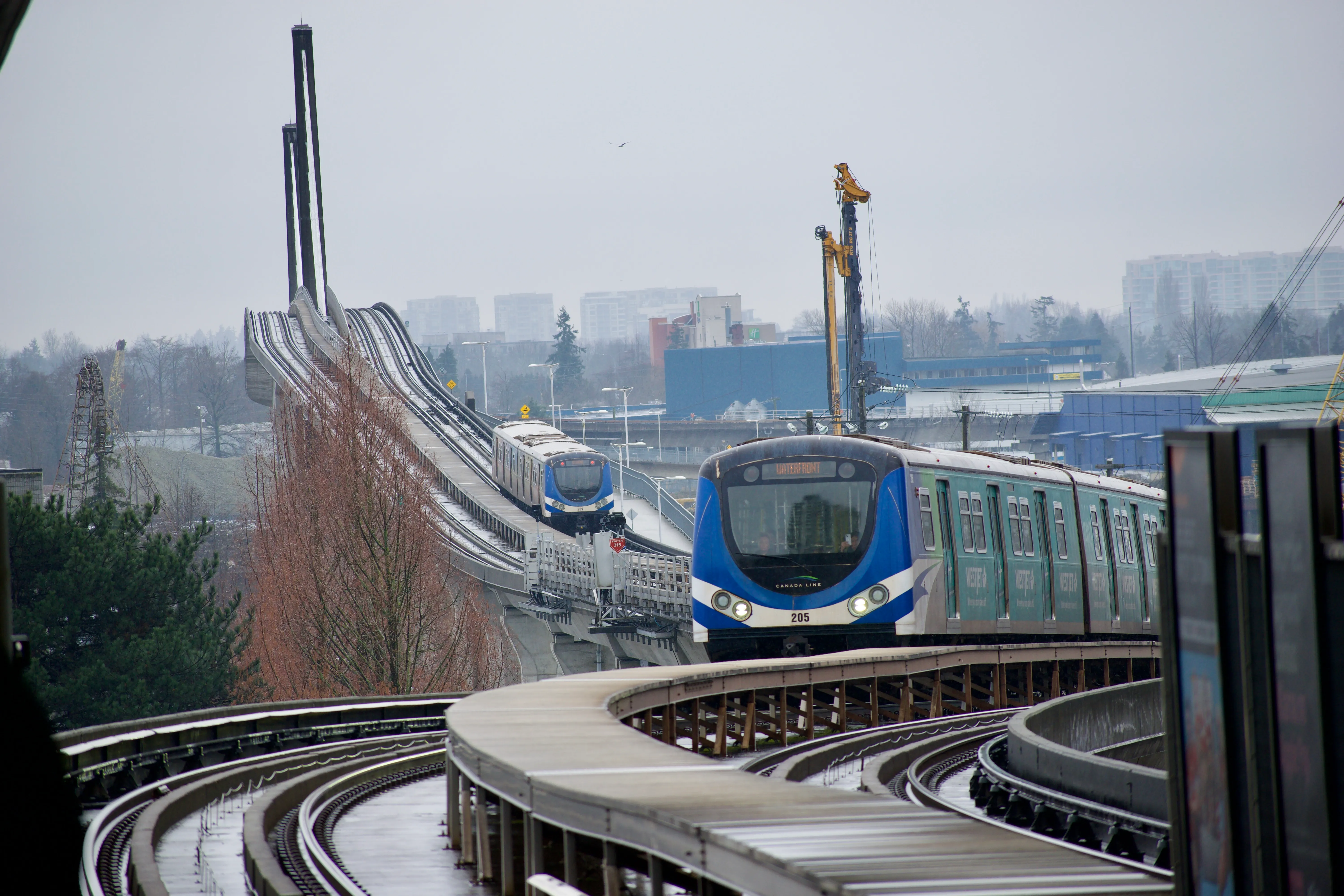 A pair of blue and silver trains travel along a curved elevated railway track.
