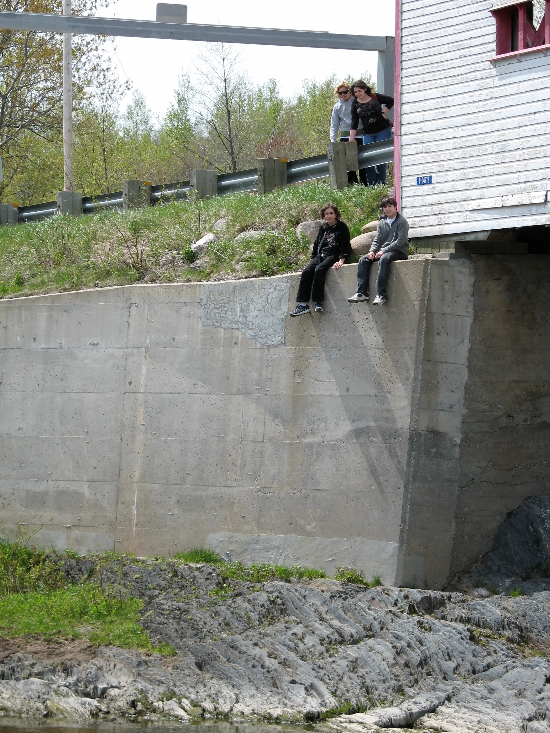 Two people sit on a tall concrete ledge which supports a covered bridge.