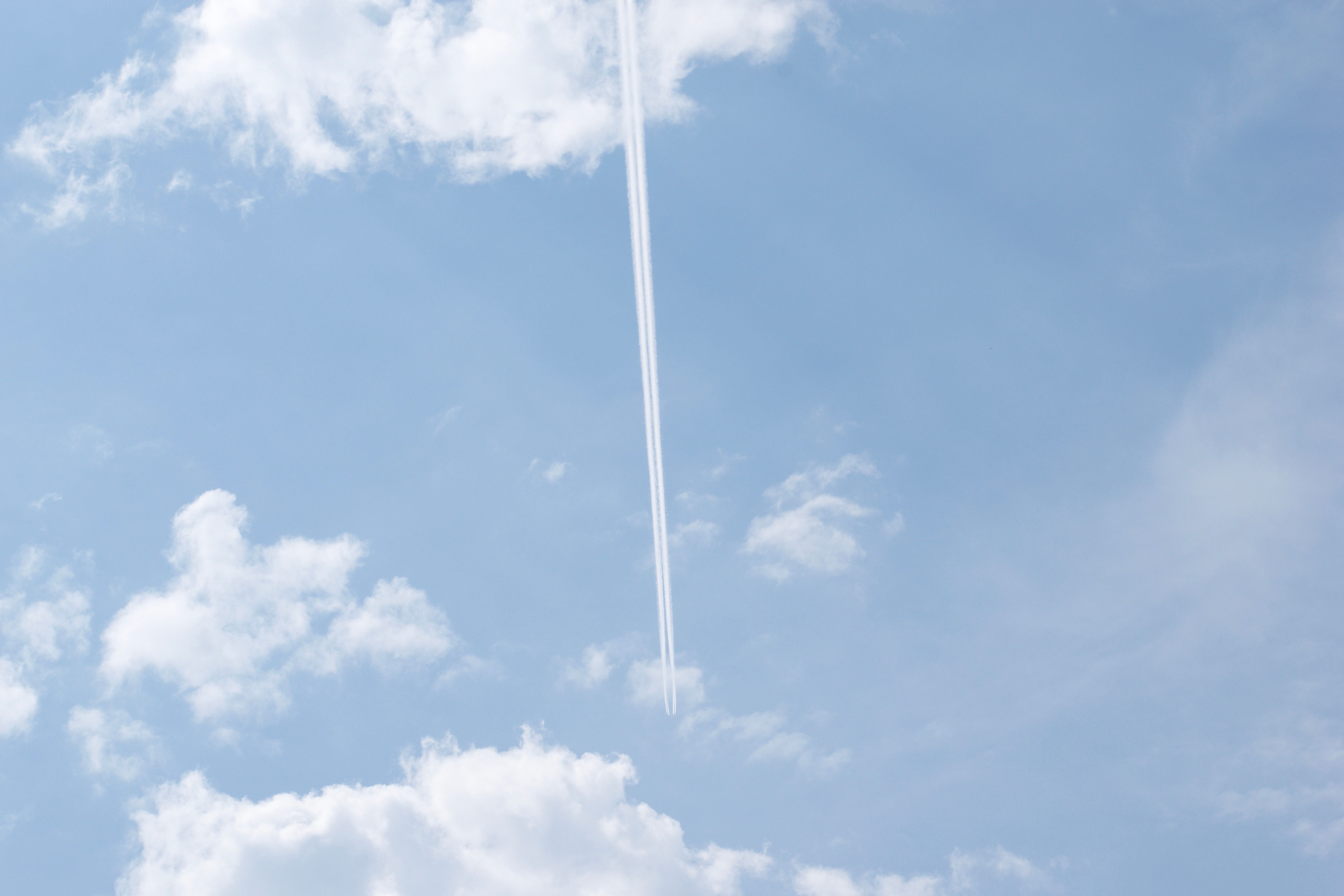 Two narrow contrails cross a blue sky with scattered clouds