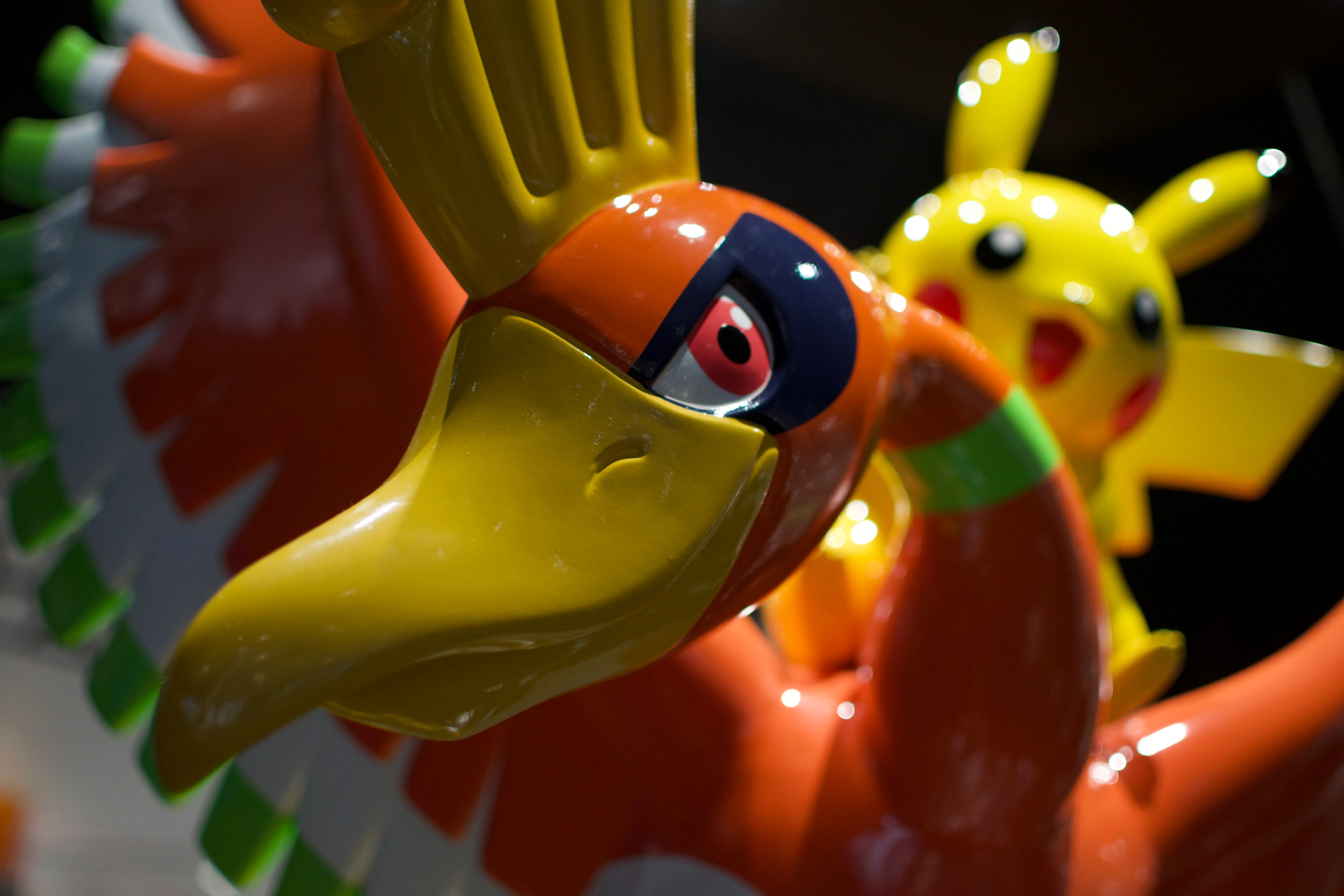 A statue of Pikachu riding Ho-oh. The photo is a close-up of on Ho-oh's head, with Pikachu and Ho-oh's wings out of focus in the background.