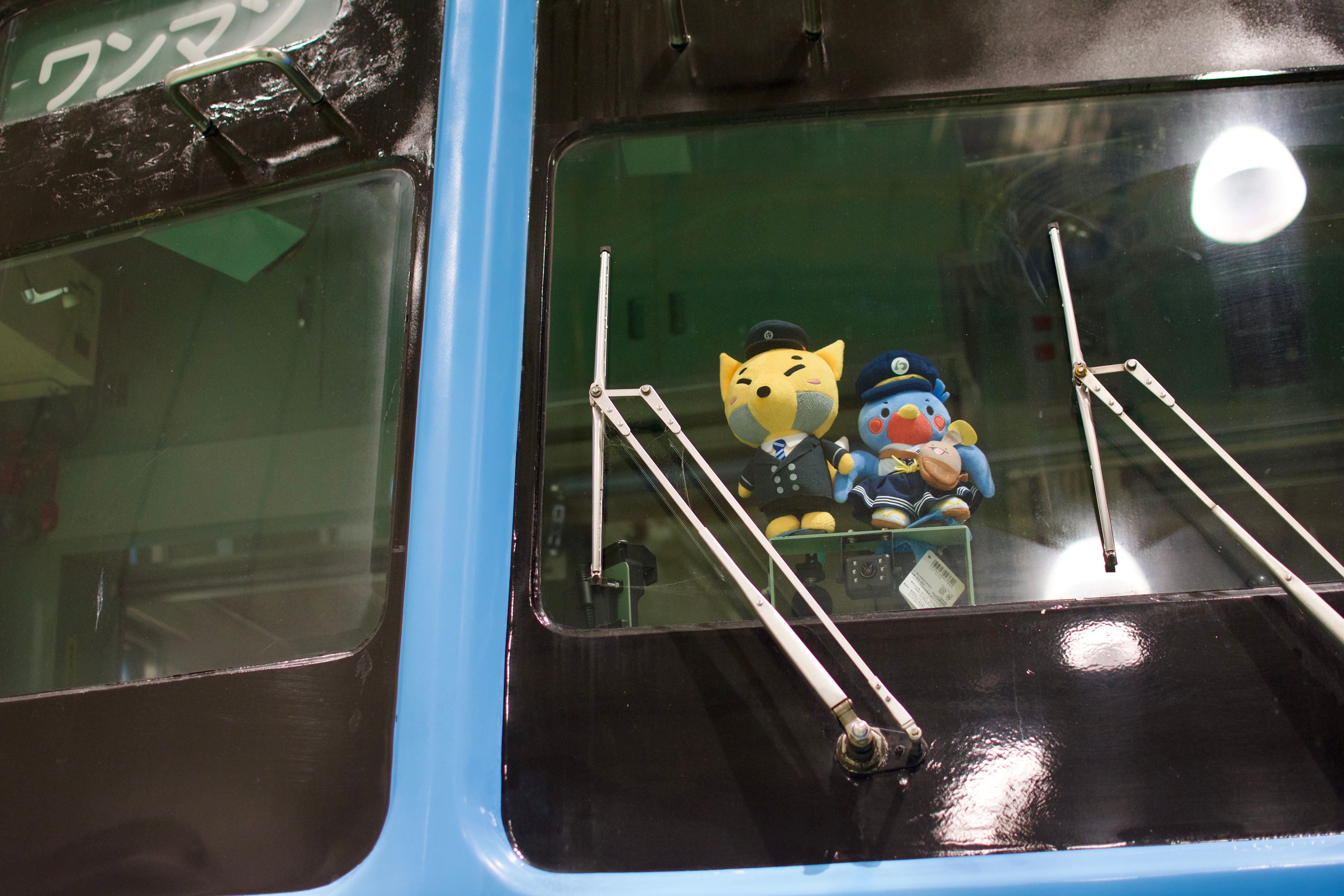 Stuffed dolls of a kitsune and a swallow, both dressed as train conductors, in the window of a train.