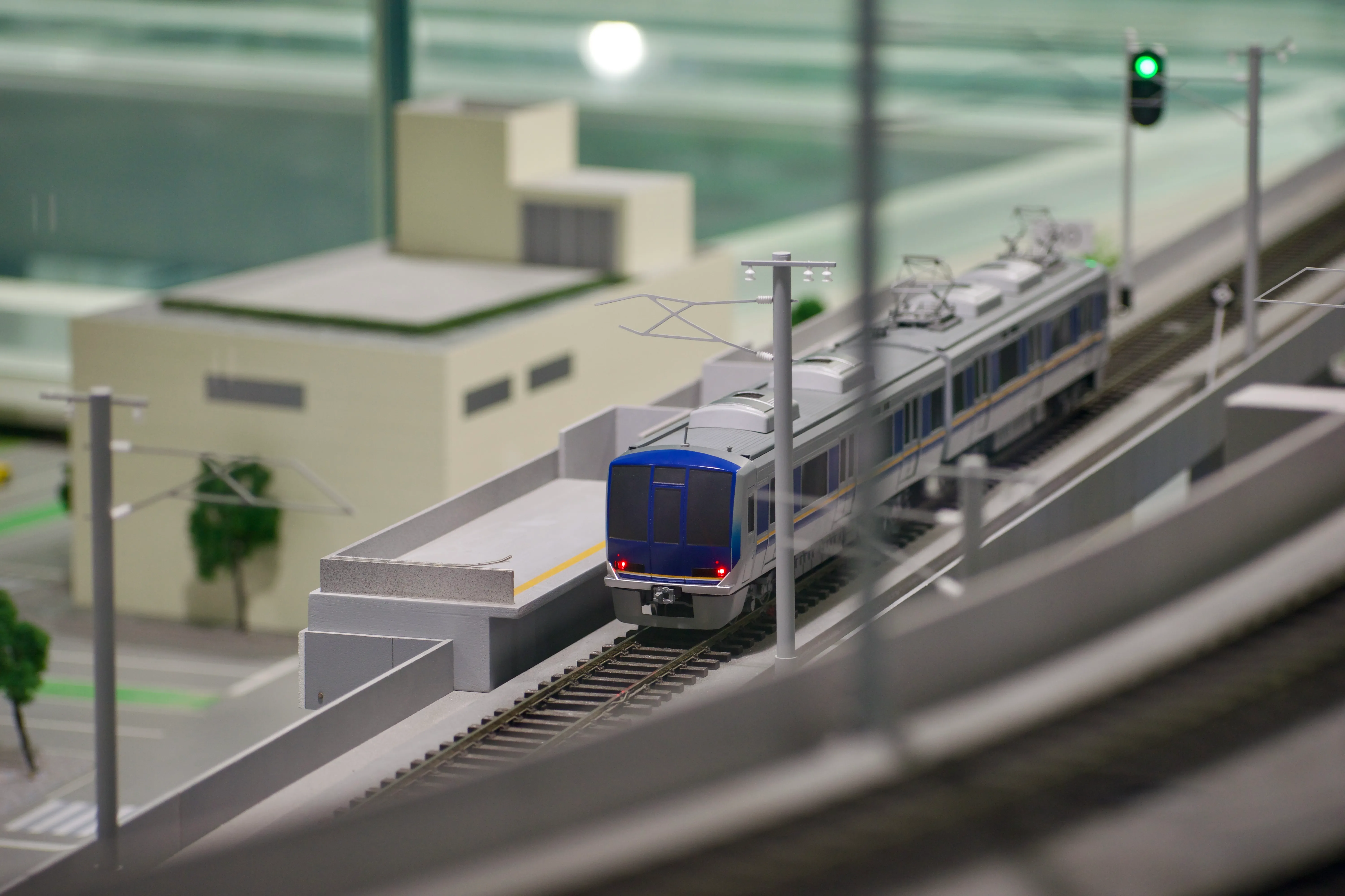 A model train on an elevated track passes a green signal light.