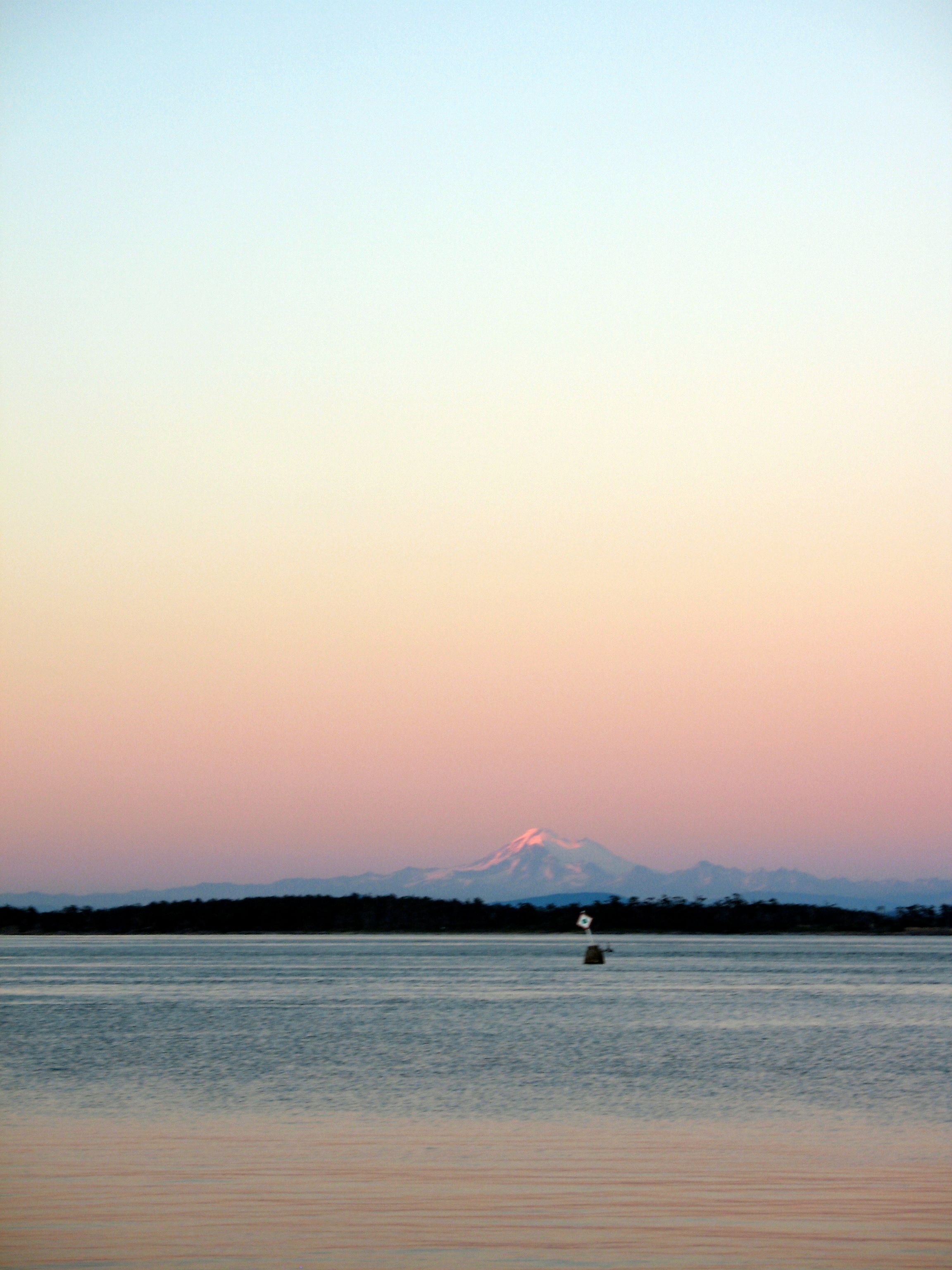 Kulshan (Mt Baker) viewed from across the Salish Sea, clad in the reddish hues of the sunset.