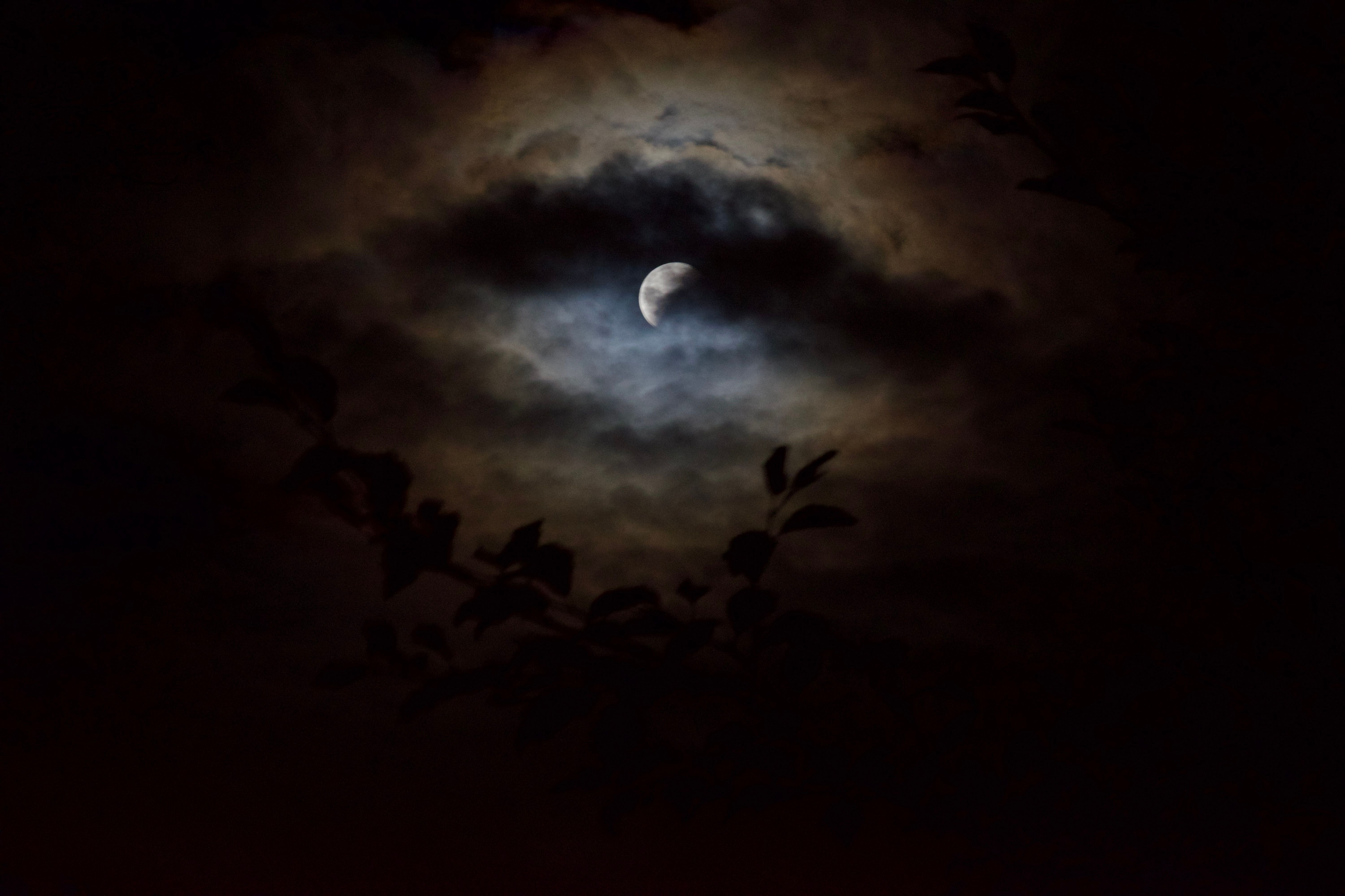 A partially-eclipsed moon illuminates a halo of clouds