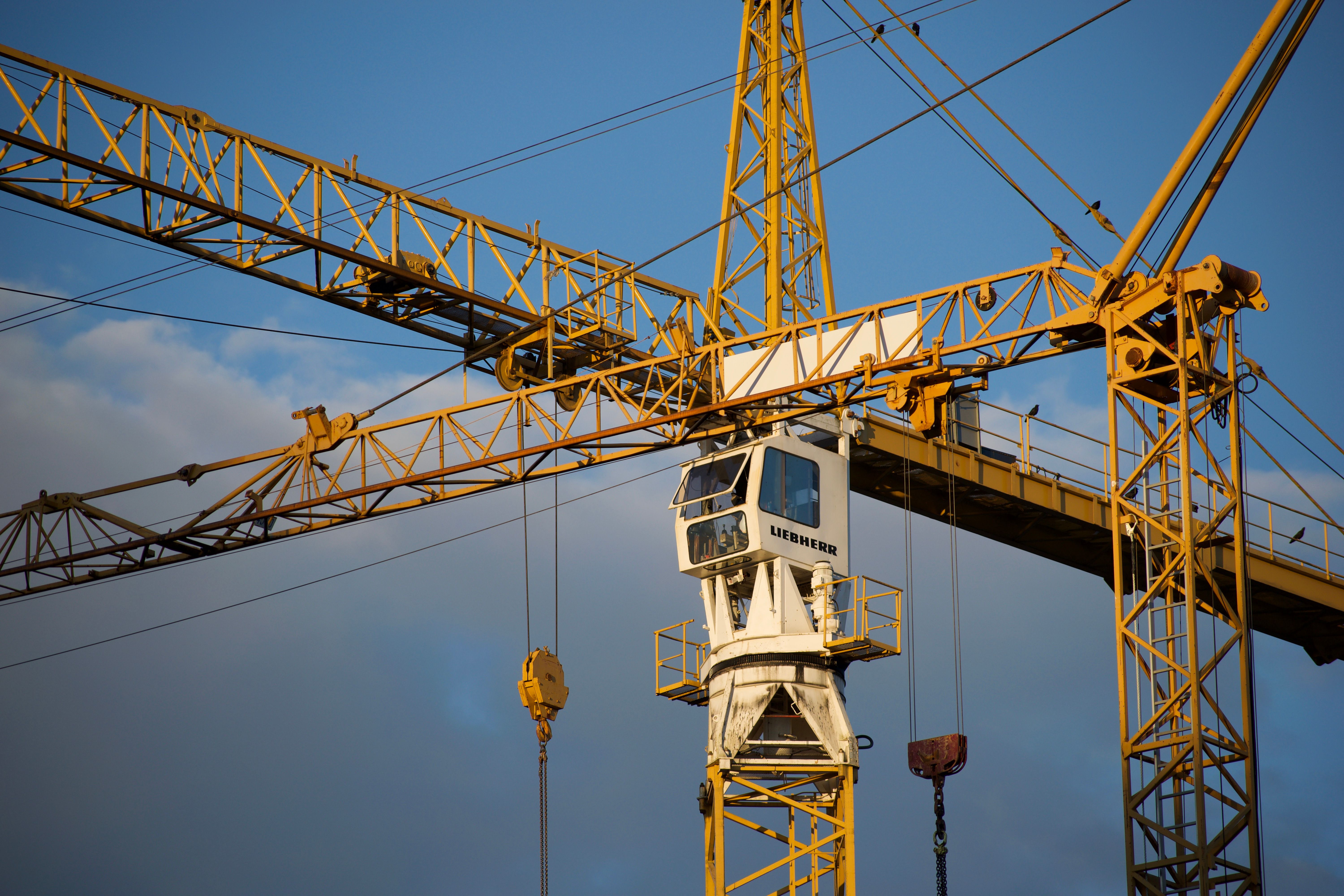 A yellow tower crane rises against a partly cloudy sky, with the focus on the operator's cab.
