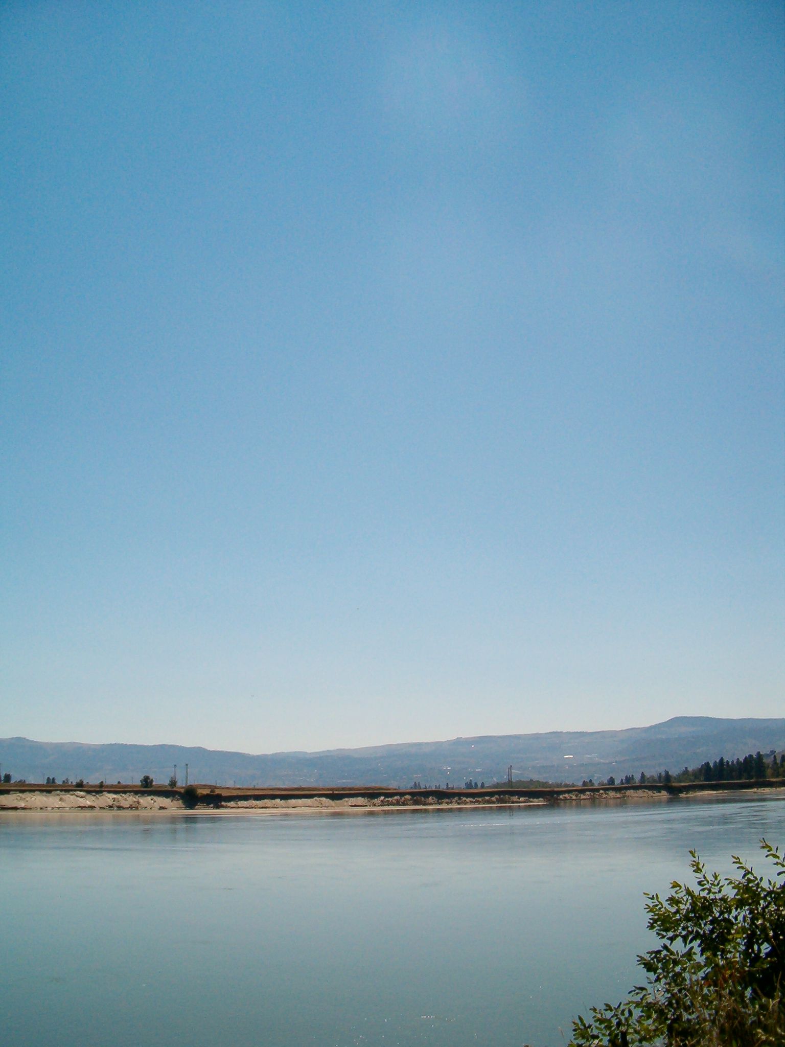 Calm water reflects a pale sky and distant hills