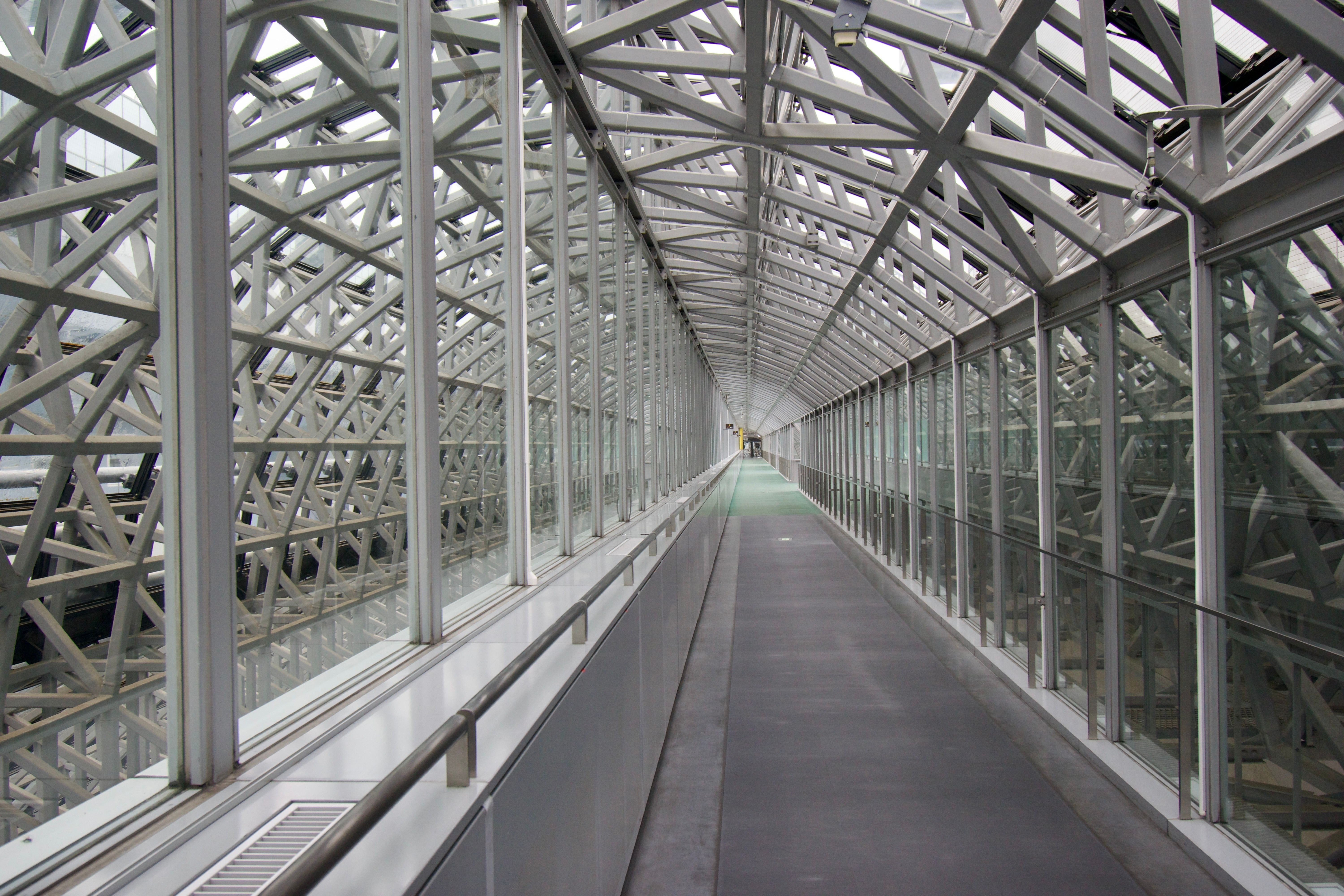 A corridor formed from glass and steel beams, illuminated by the natural light of a cloudy day.