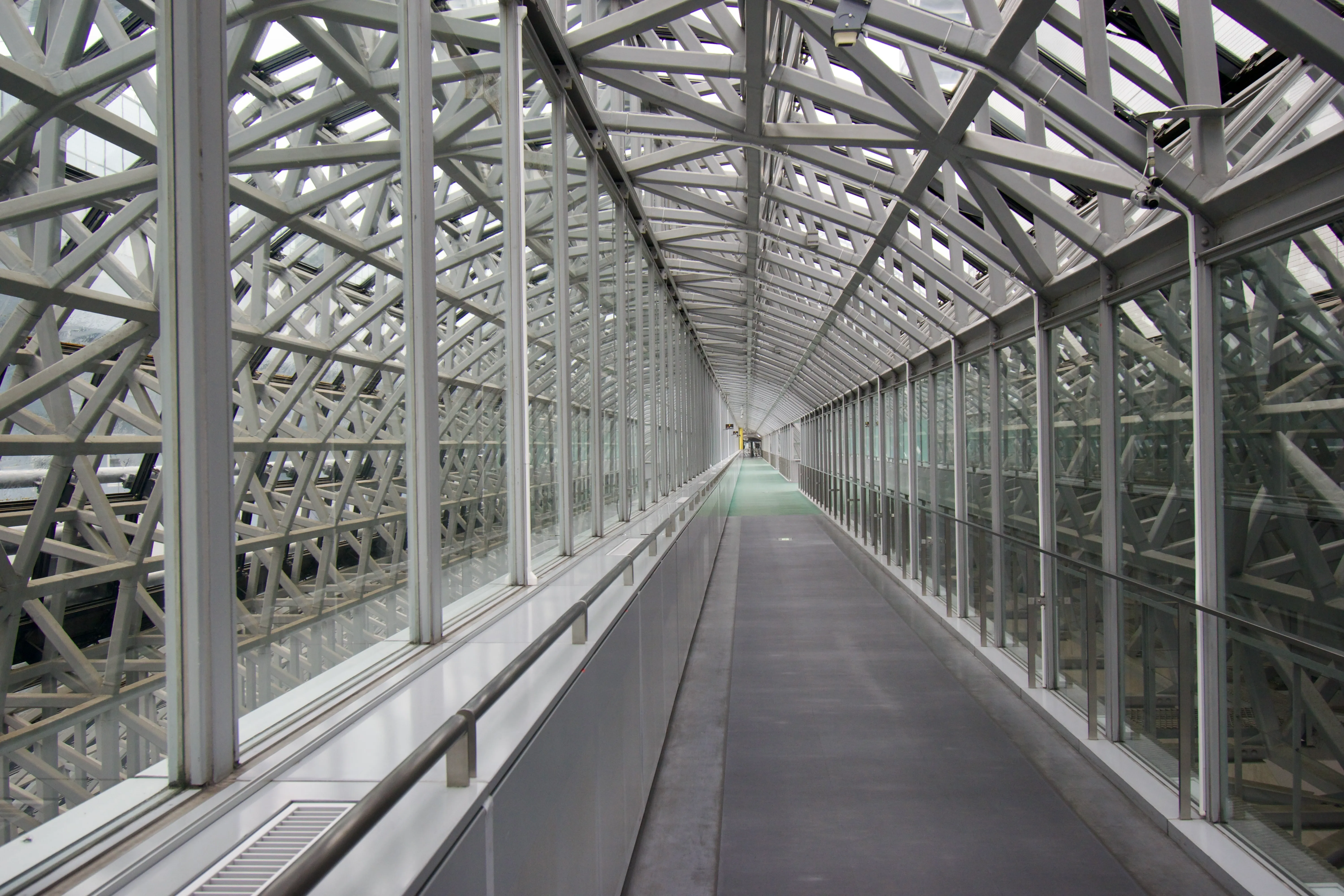 A corridor formed from glass and steel beams, illuminated by the natural light of a cloudy day