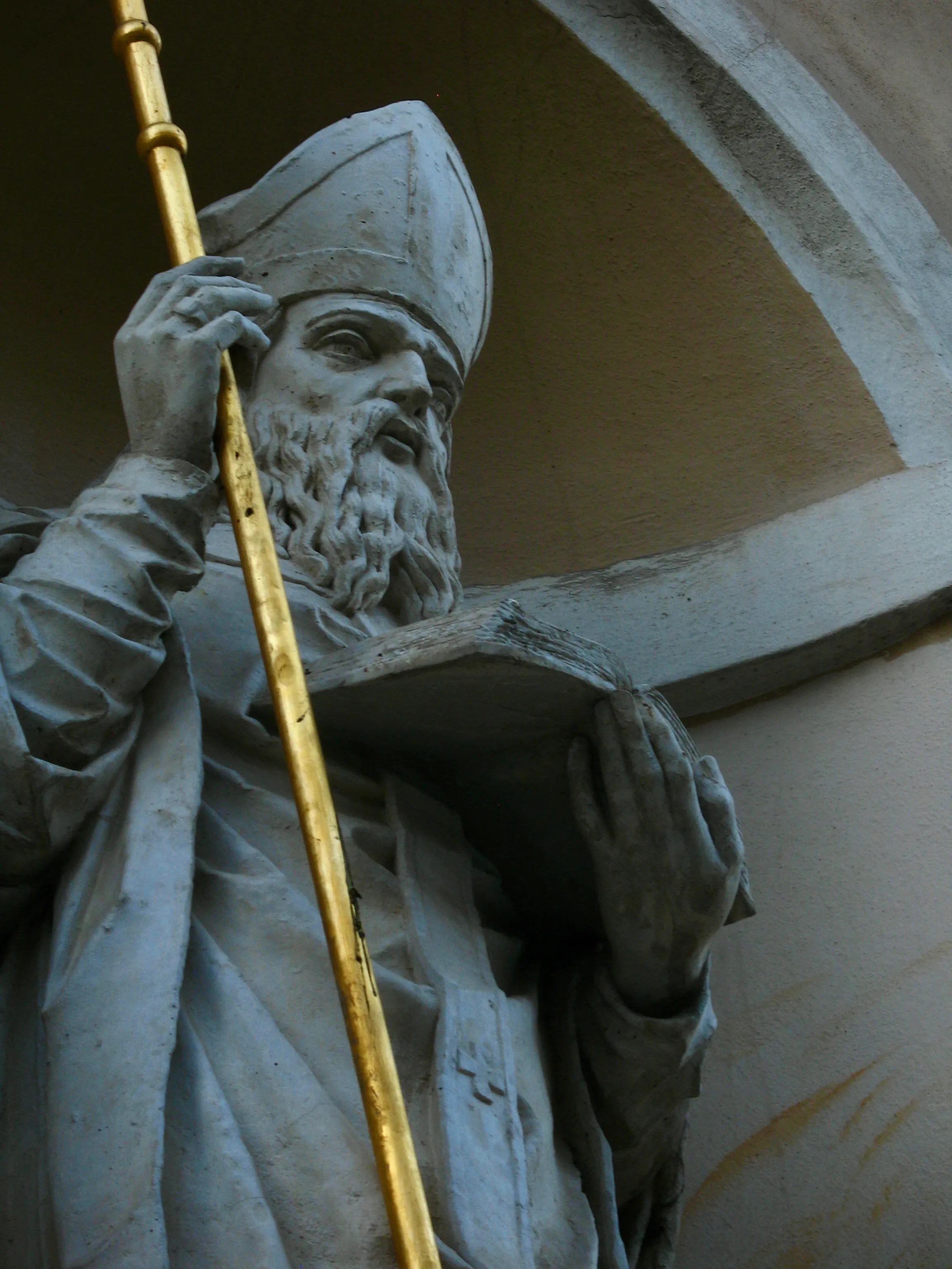 A stone statue of a bishop holding a book and a golden staff