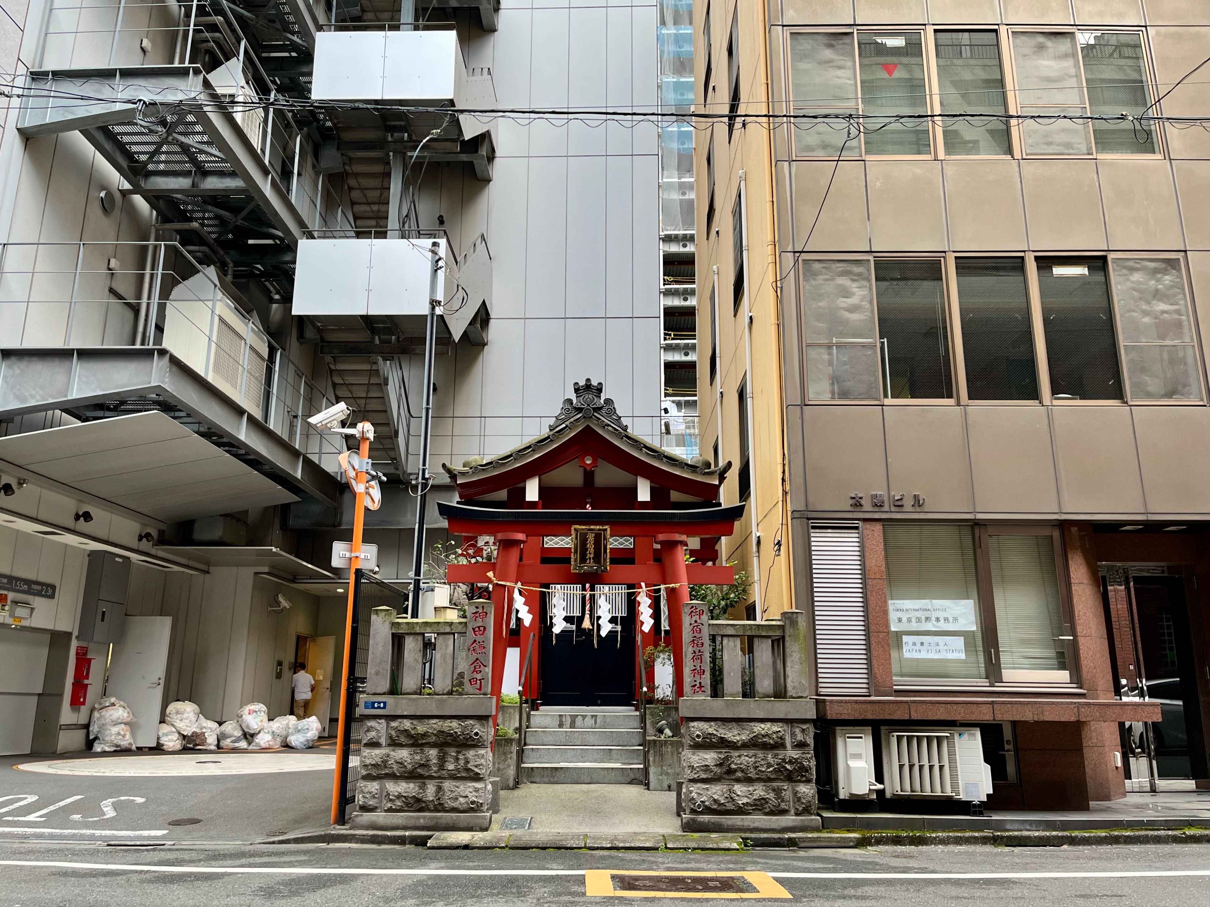 A small shrine sandwiched between large office buildings on a side street in Tōkyō.
