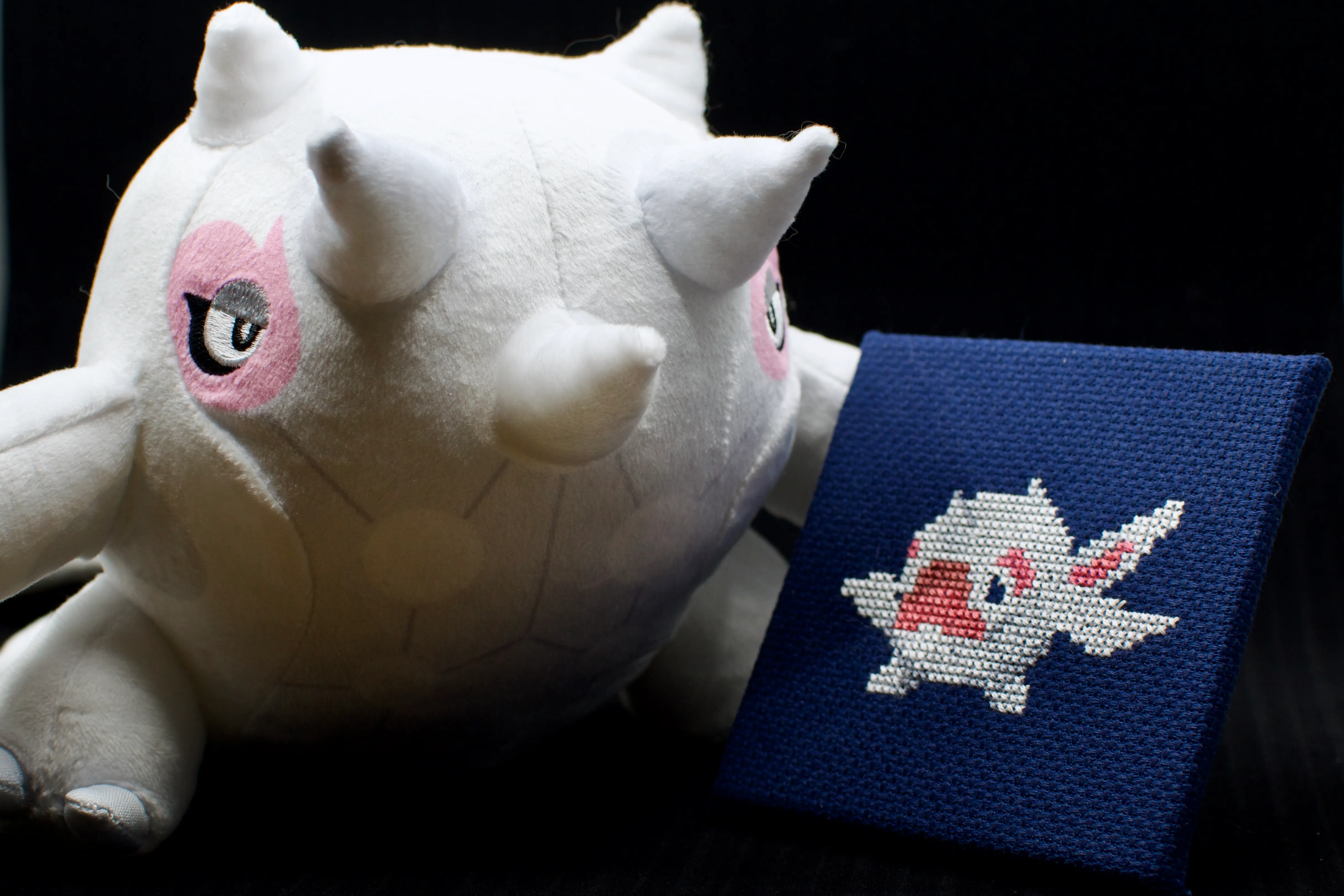 A cross-stitch of the Terra Whale Pokémon Cetoddle next to a stuffed animal of its evolved form Cetitan