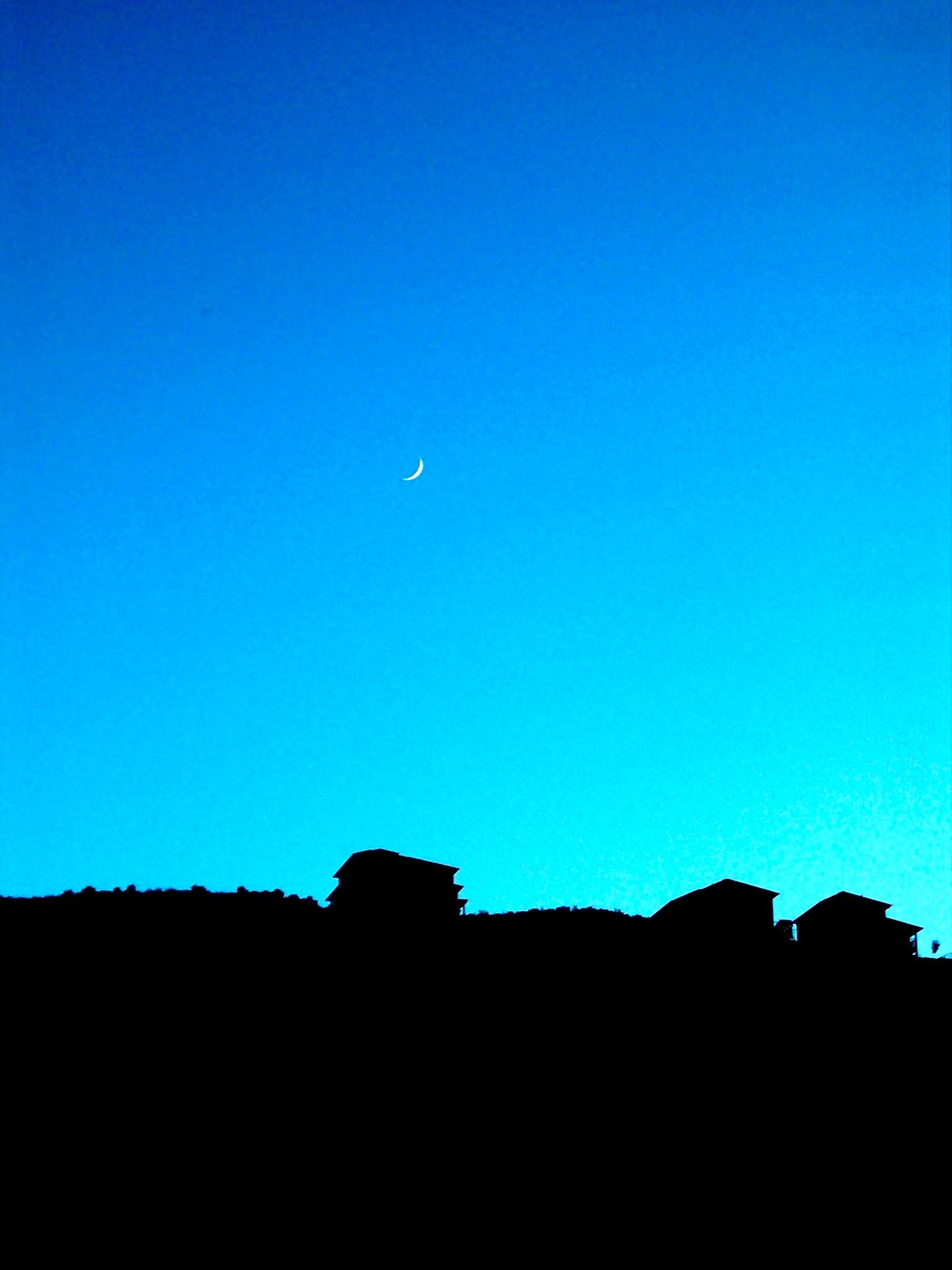 The crescent moon hovers over a fully-silhouetted house on a hill.