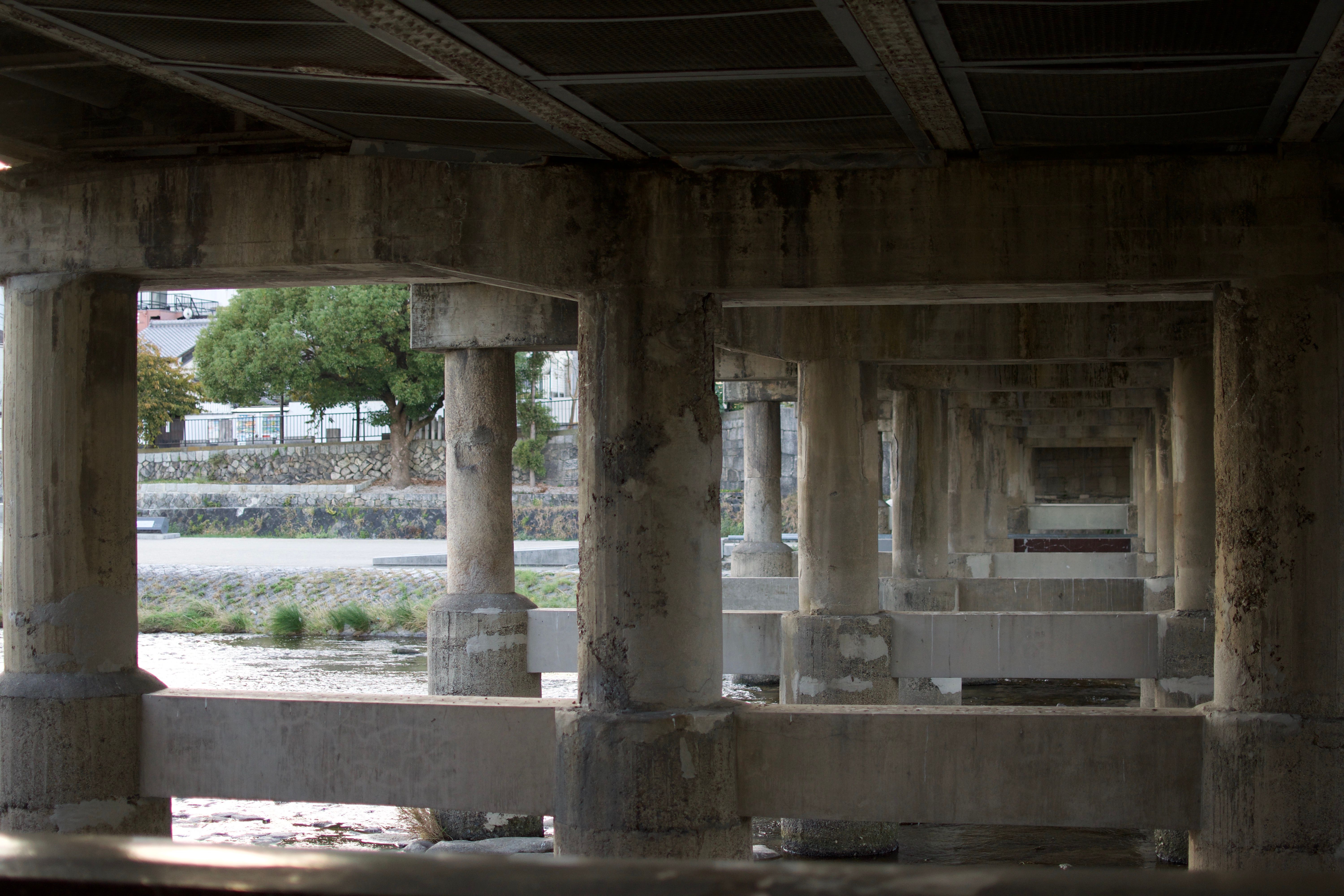 Concrete pillars supporting a bridge. There are at least six sets, each consisting of three pillars connected by a horizontal concrete beam.