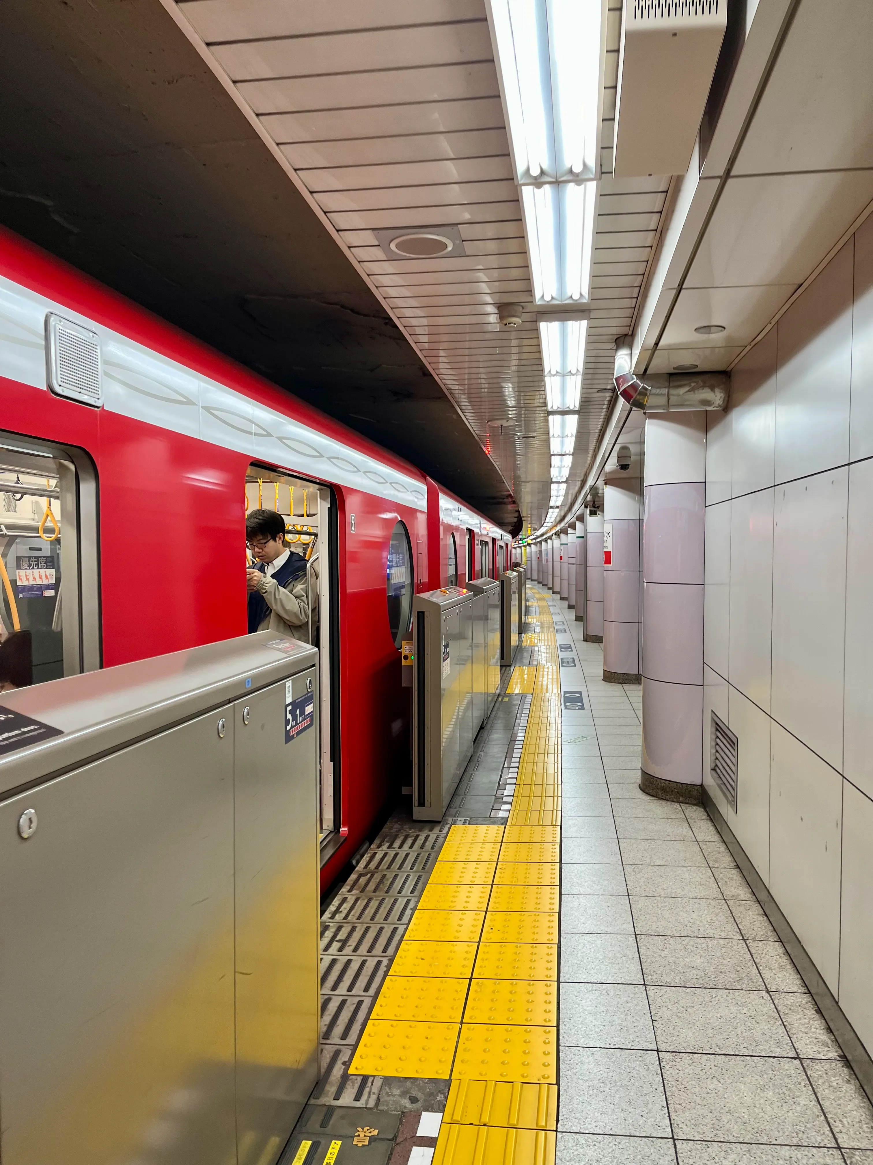 A red subway car stopped at a long, empty platform that curves into the distance