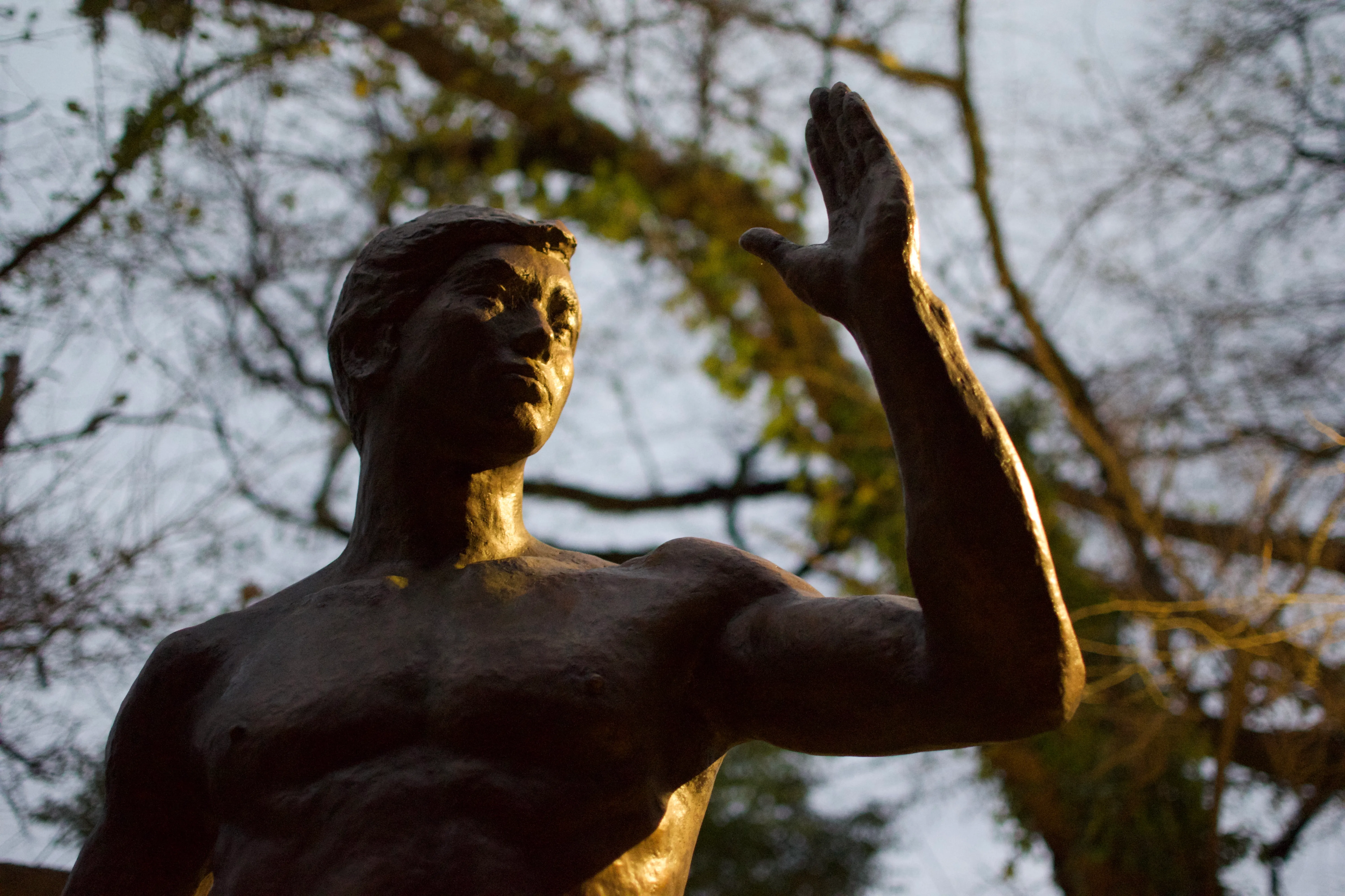 A statue of an athletic young man raising his forearm is dramatically illuminated from one side