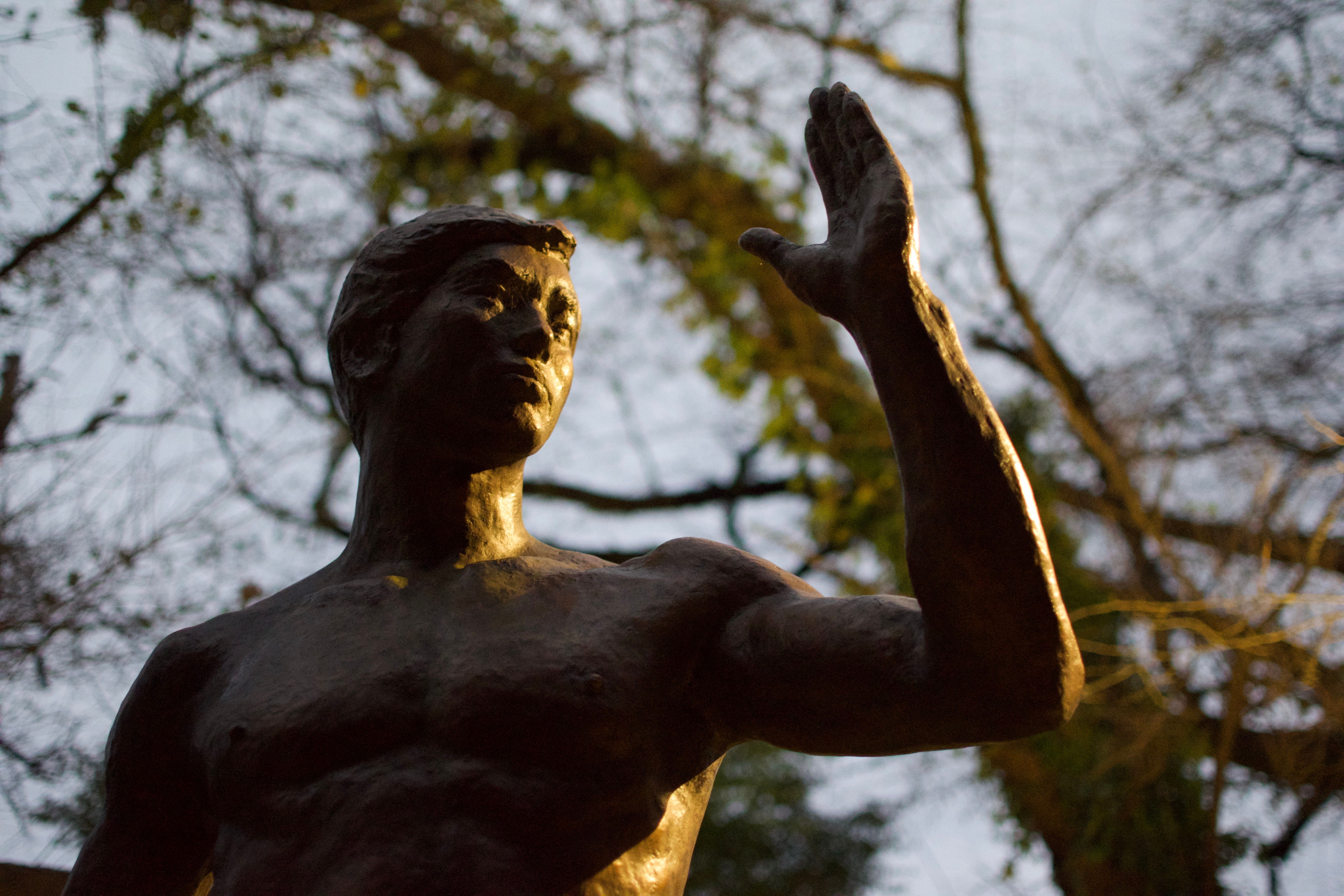 A statue of an athletic young man raising his forearm is dramatically illuminated from one side.