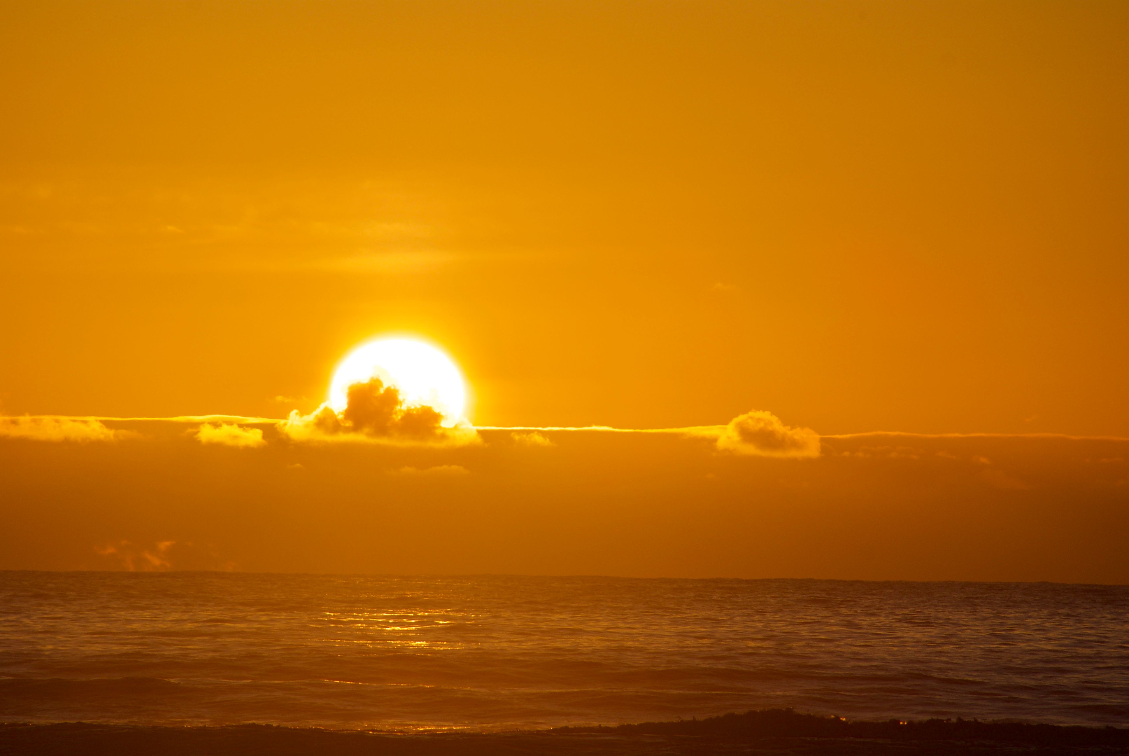 The sun sets below a layer of clouds on the ocean horizon. The entire photo is bathed in a golden hue.