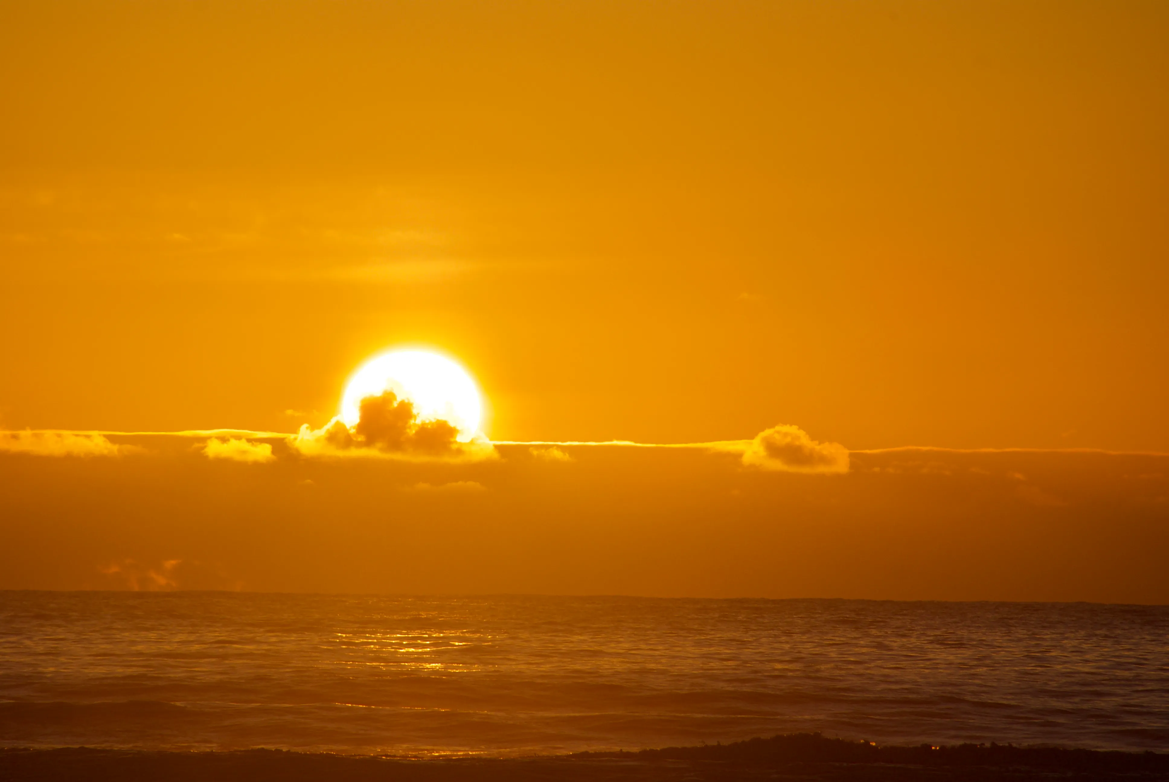 The sun sets below a layer of clouds on the ocean horizon. The entire photo is bathed in a golden hue.