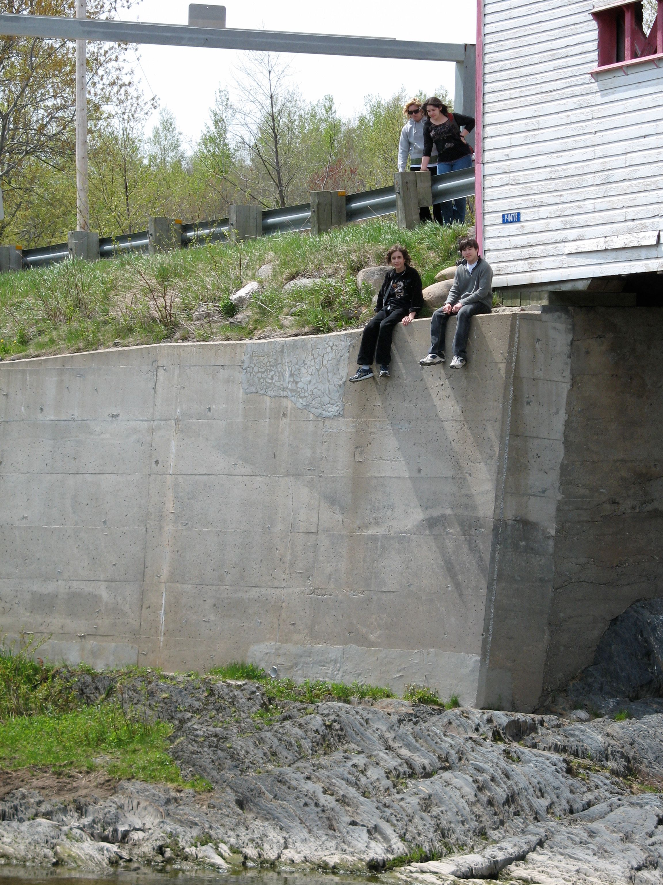Two people sit on a tall concrete ledge which supports a covered bridge.