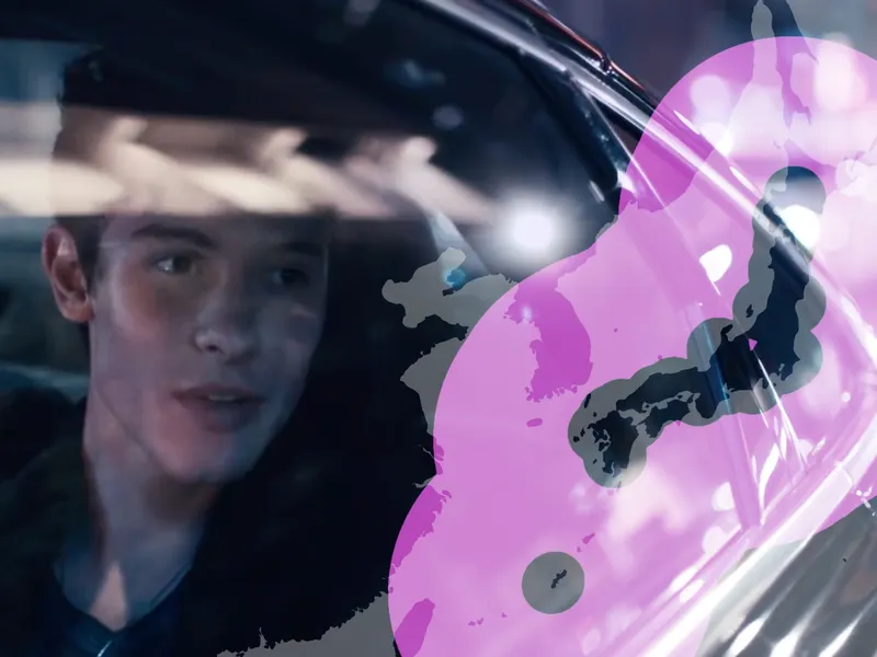 A still from the music video to "Lost in Japan" composited with a map of Japan and its surroundings. A young man sits in the back seat of a car driving through a city at night, looking wistfully out the window. His gaze is directed to the right of the frame, where the map is, but the look in his eyes is far more distant.