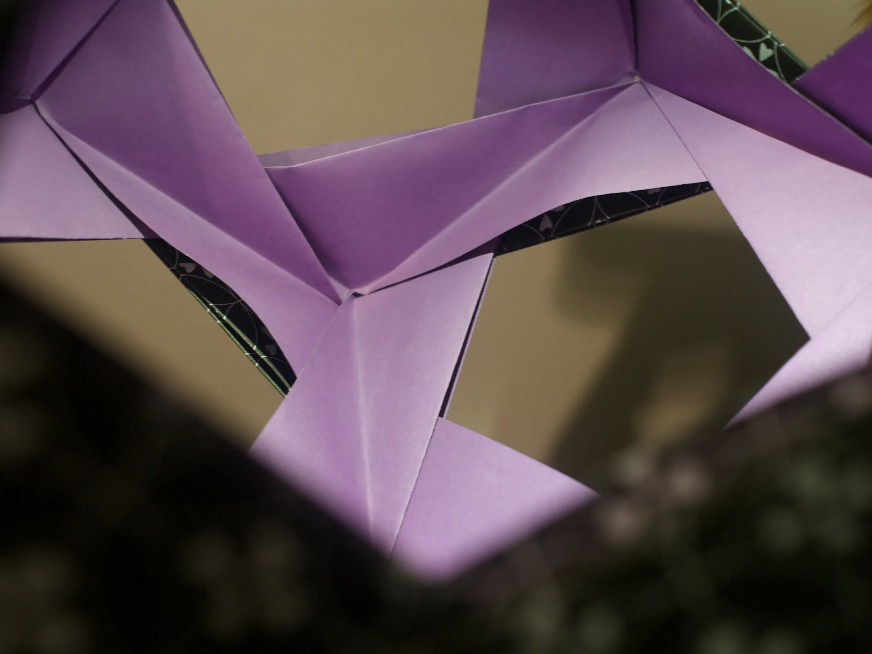 A close-up photo of the interior of an origami dodecahedral skeleton. The origami paper is solid purple on the inside and is black on the outside with a pattern of flowers and overlapping circles.