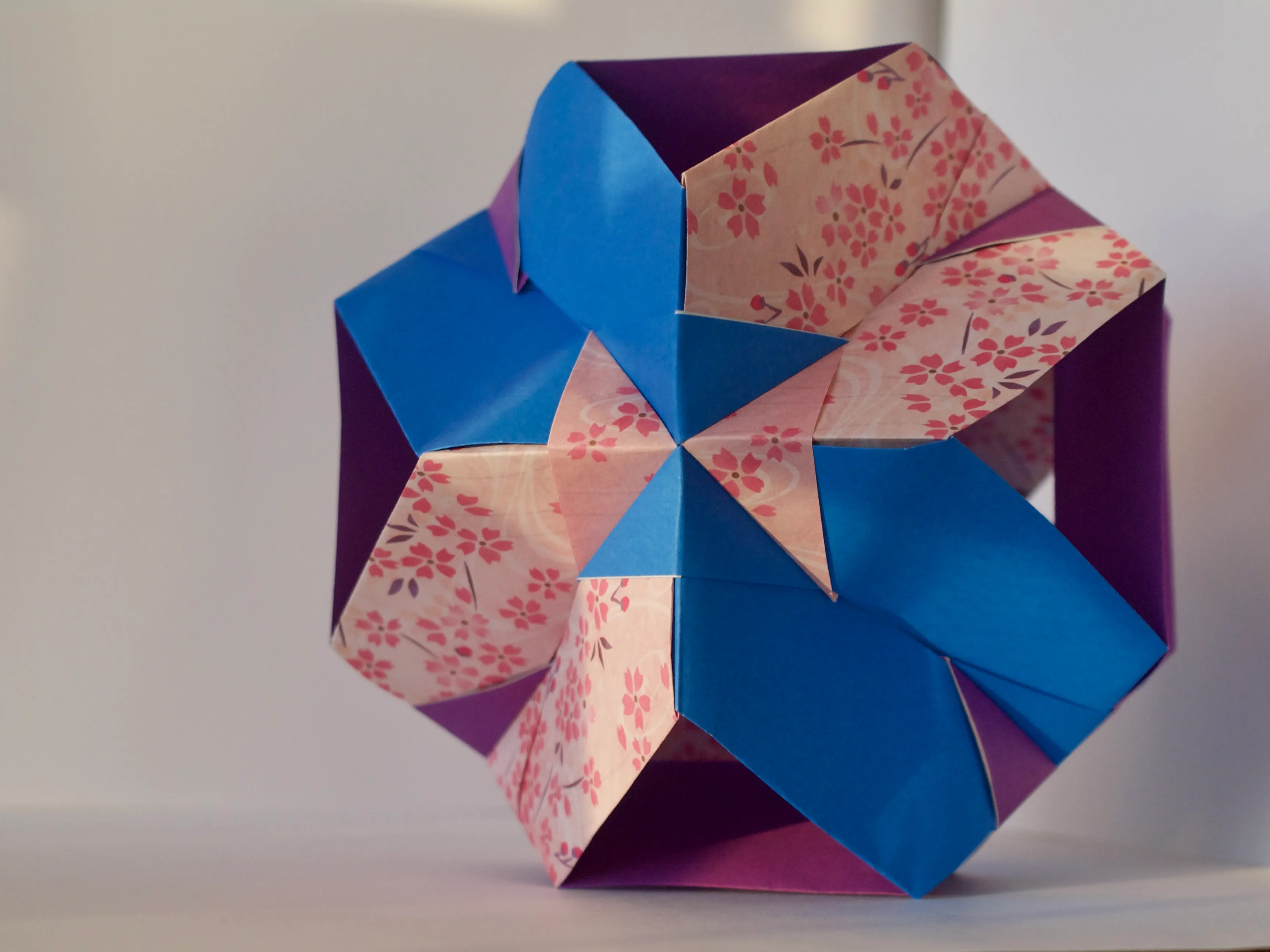 A photo of a sun-dappled moduler origami module made from blue, purple, and pink cherry blossom origami paper.