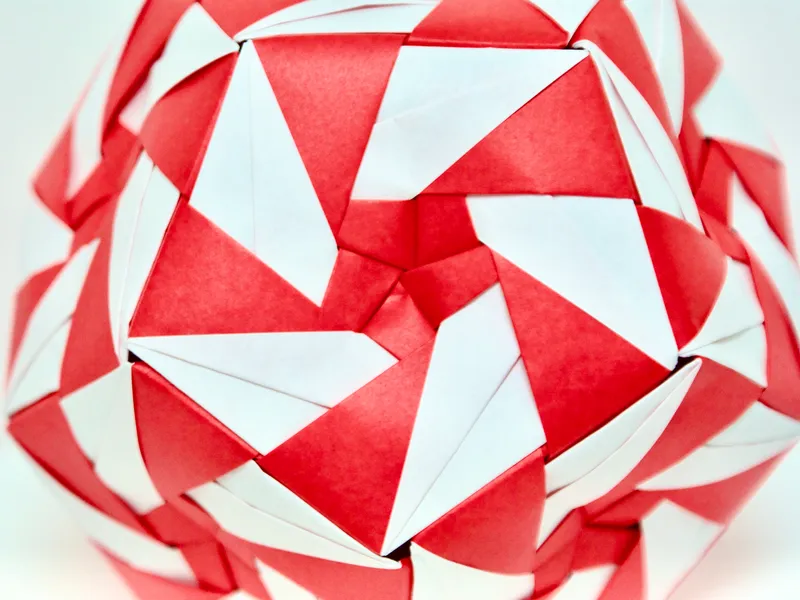 A close-up photo of an origami dodecahedron with a red-and-white pinwheel pattern on each face.