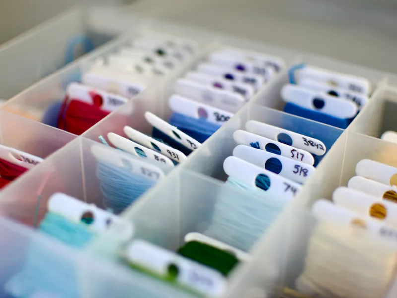 A close-up photo of a plastic box filled with labeled bobbins of lots of different DMC thread colours.