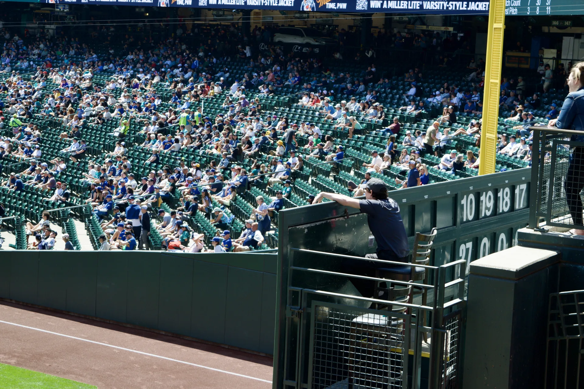 A young, bored-looking person sits on a chair and rests their arms on the stadium scoreboard.